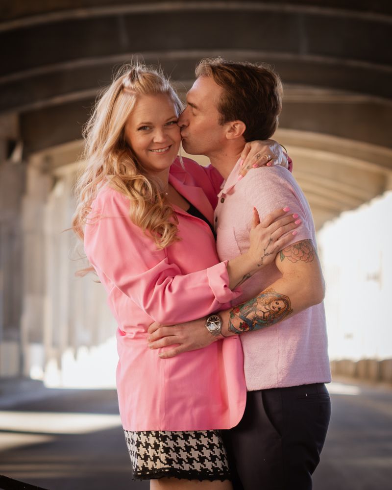 A couple embraces and shares a romantic moment under a concrete bridge structure in a photo series.