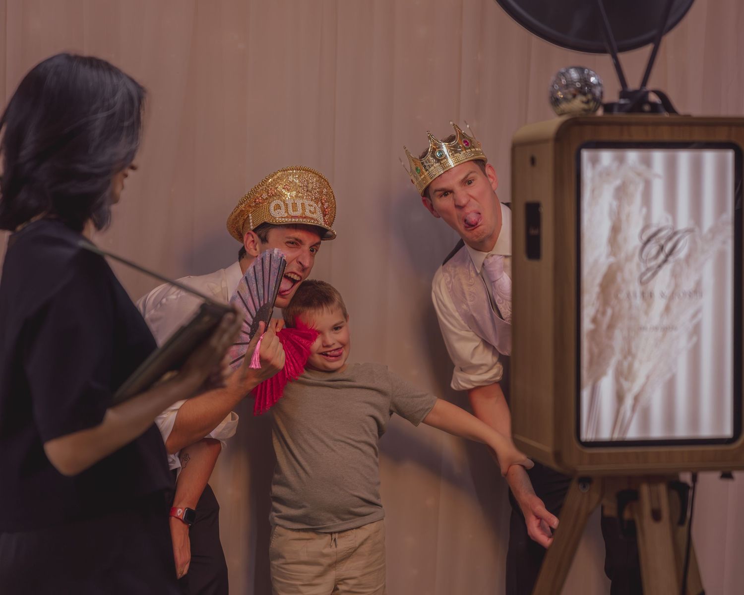 Group of people posing with fun props and crowns at a photo booth during a celebration event.