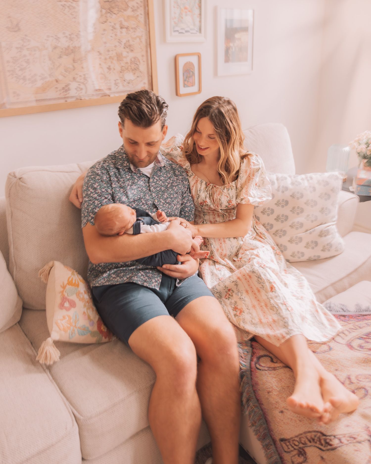 A couple sitting on a couch smiling at their newborn baby in a cozy, warmly decorated living room.