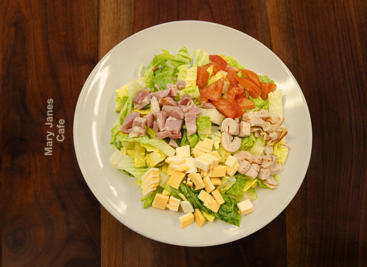 Fresh chef salad with ham, chicken, cheese, tomatoes, and lettuce on a white plate at Mary Janes Cafe.
