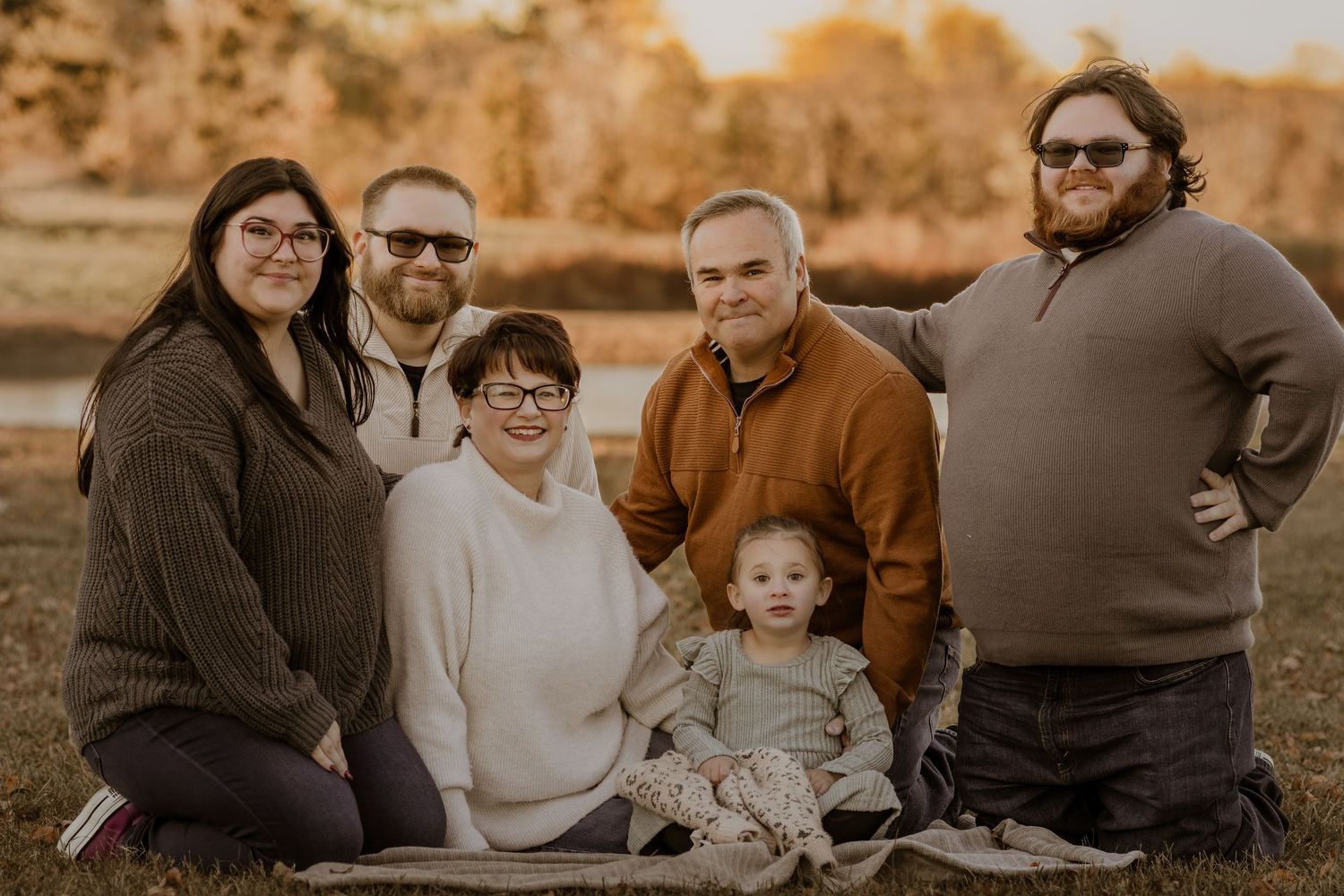 Family of six smiling together on a blanket in a golden autumn field during an outdoor photo session.