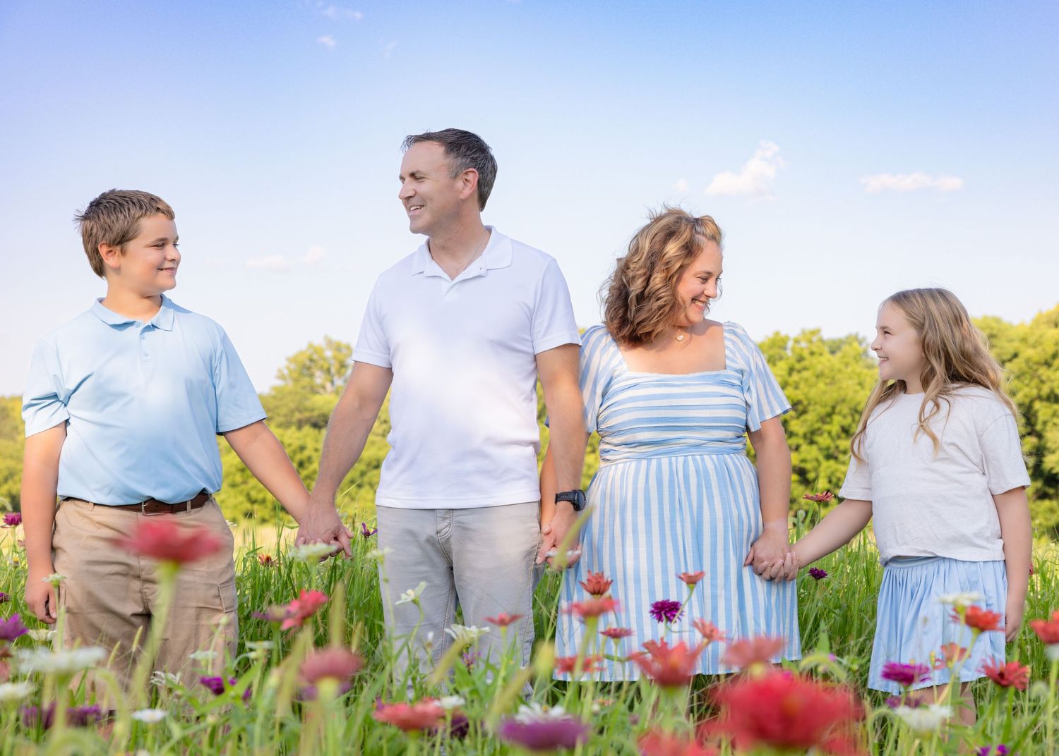 Family of four holding hands in a wildflower meadow under a blue sky on a sunny day.