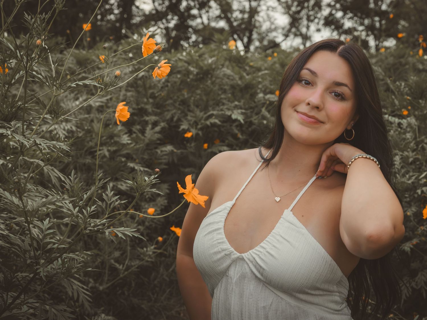 Young woman in white halter top smiling among orange wildflowers in a garden.