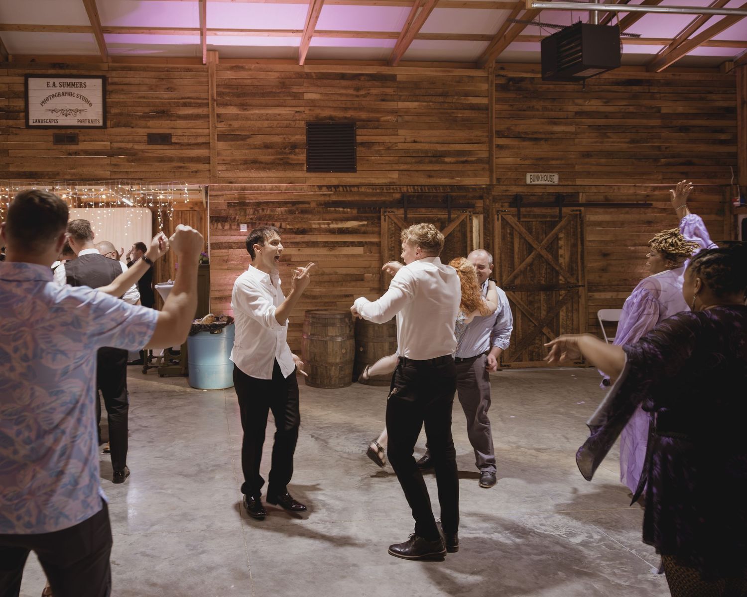 Guests enjoy energetic dancing at a rustic wooden barn wedding reception.