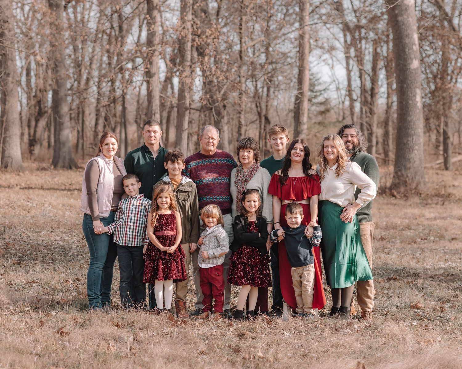 A large group of people in coordinated red, green, and neutral colored outfits pose together in a wooded setting.