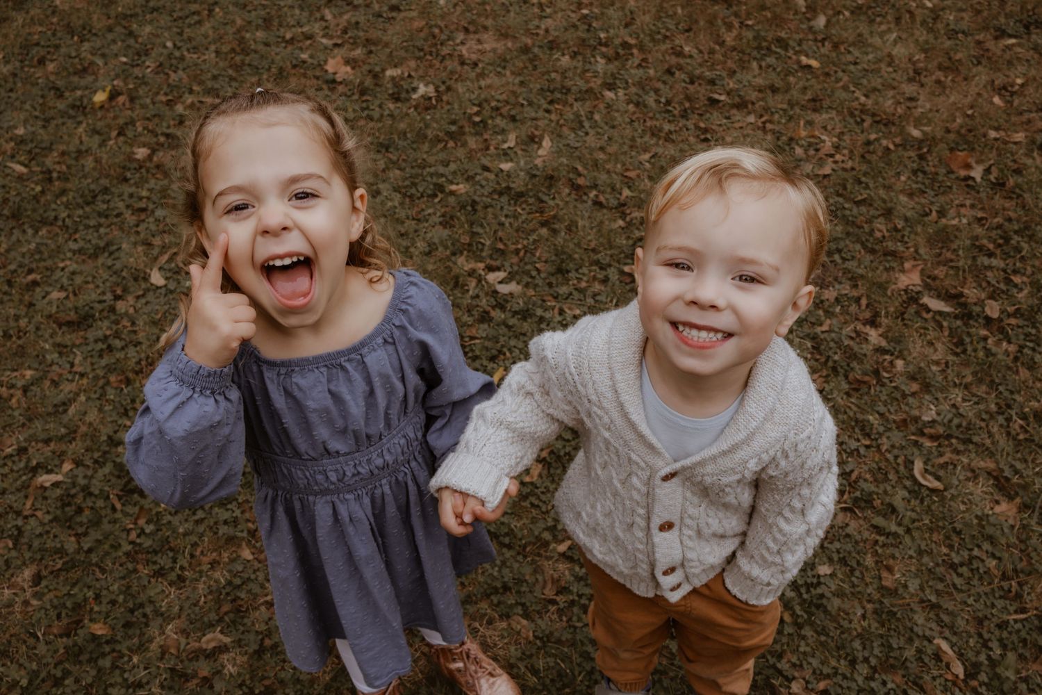 Two young children laugh and play together on fallen autumn leaves.