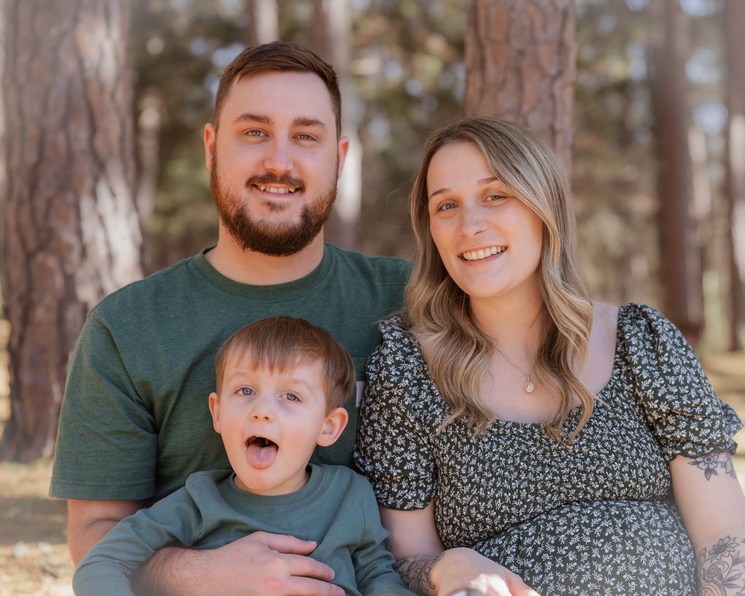 Family maternity photos in a forest setting with everyone wearing coordinating green outfits.