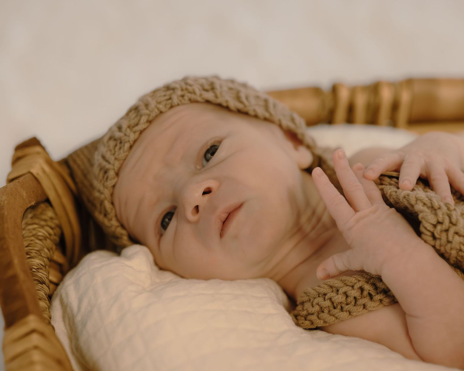 Awake newborn baby in a knit hat lying in a wicker basket looking up curiously.