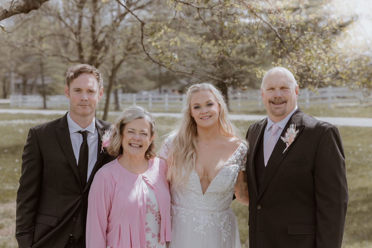 Wedding party of four posing outdoors, bride in white gown flanked by family in formal attire.