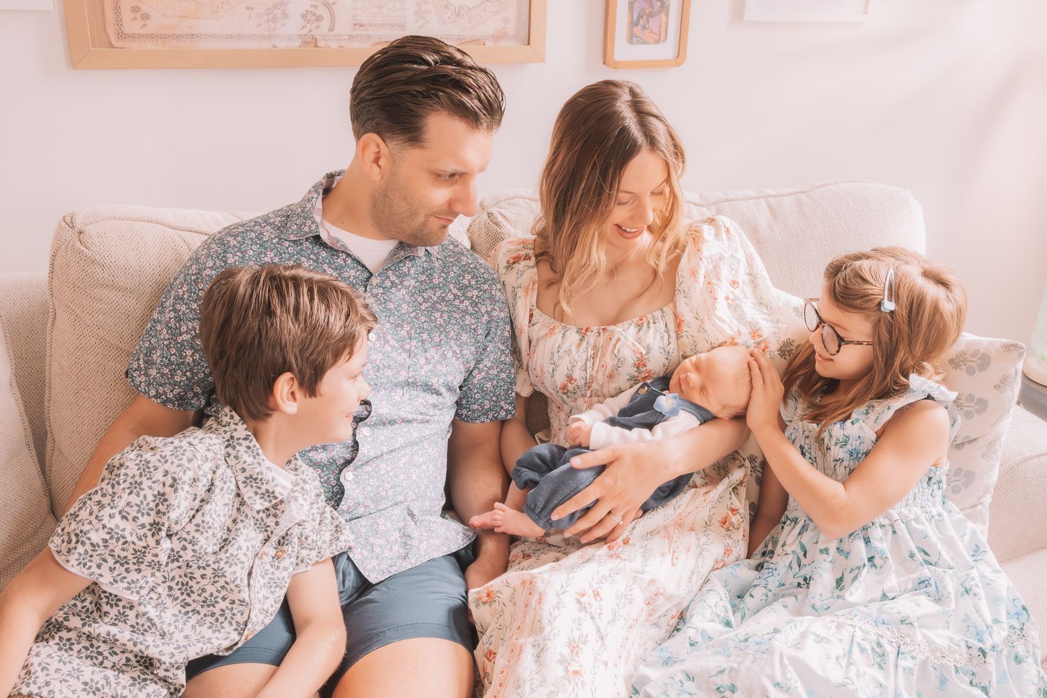 Family of five sitting on a couch, parents with two children and a newborn baby in a bright, cozy living room.