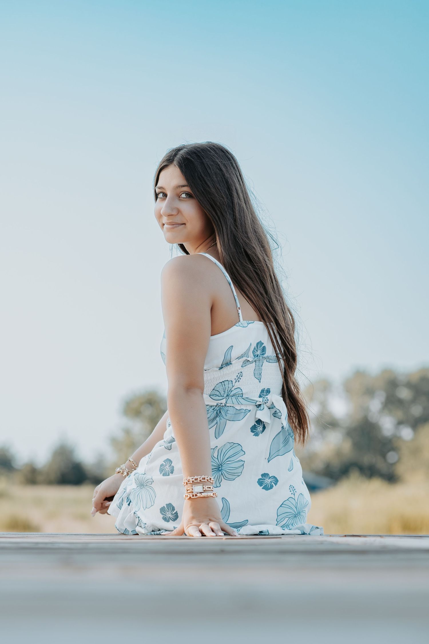 Someone wearing a floral blue and white sundress sits outdoors on a sunny day, turning to look over their shoulder.