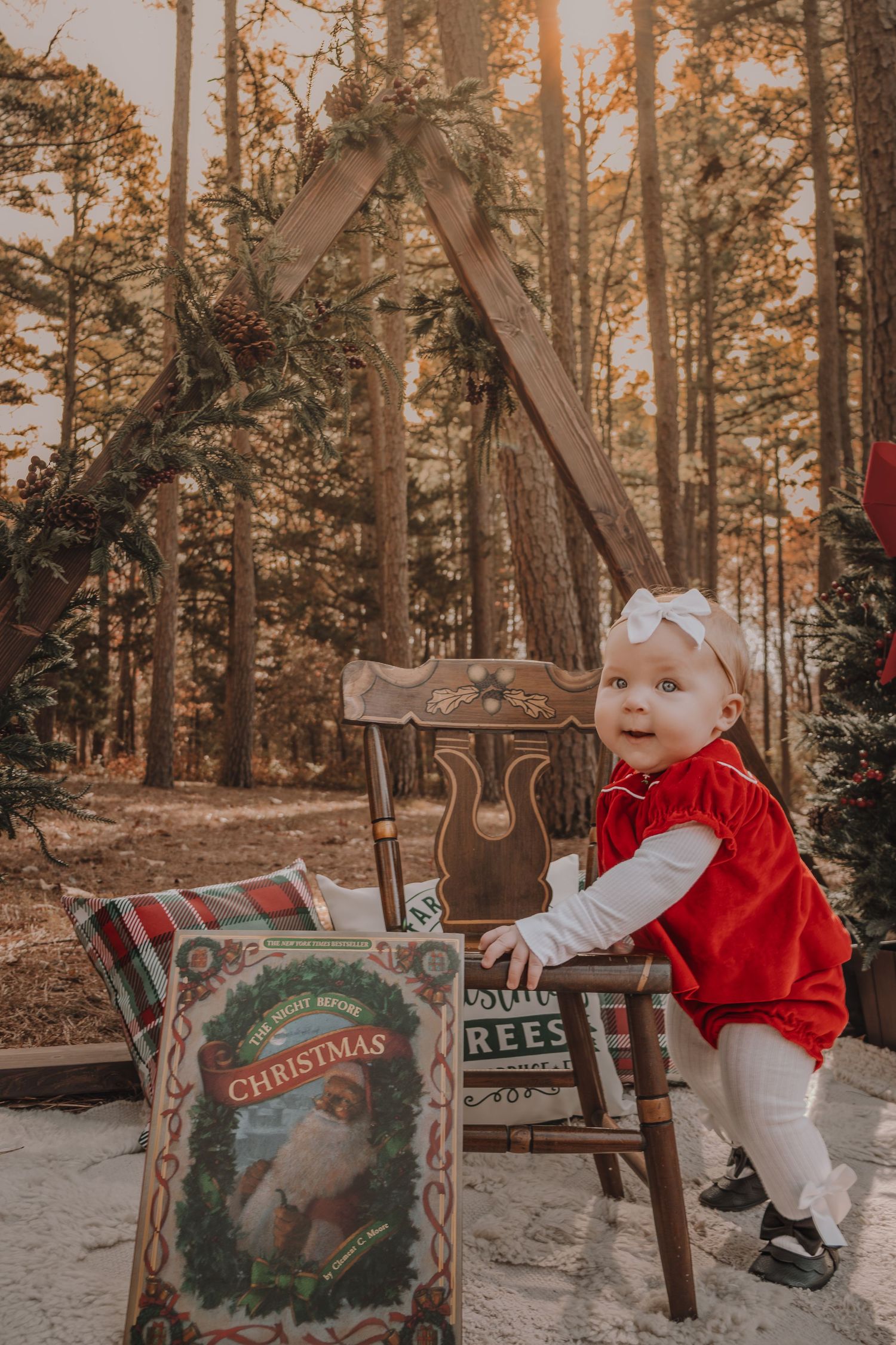 Holiday photo session in a forest setting with rustic wooden chair and Christmas decor at sunset.