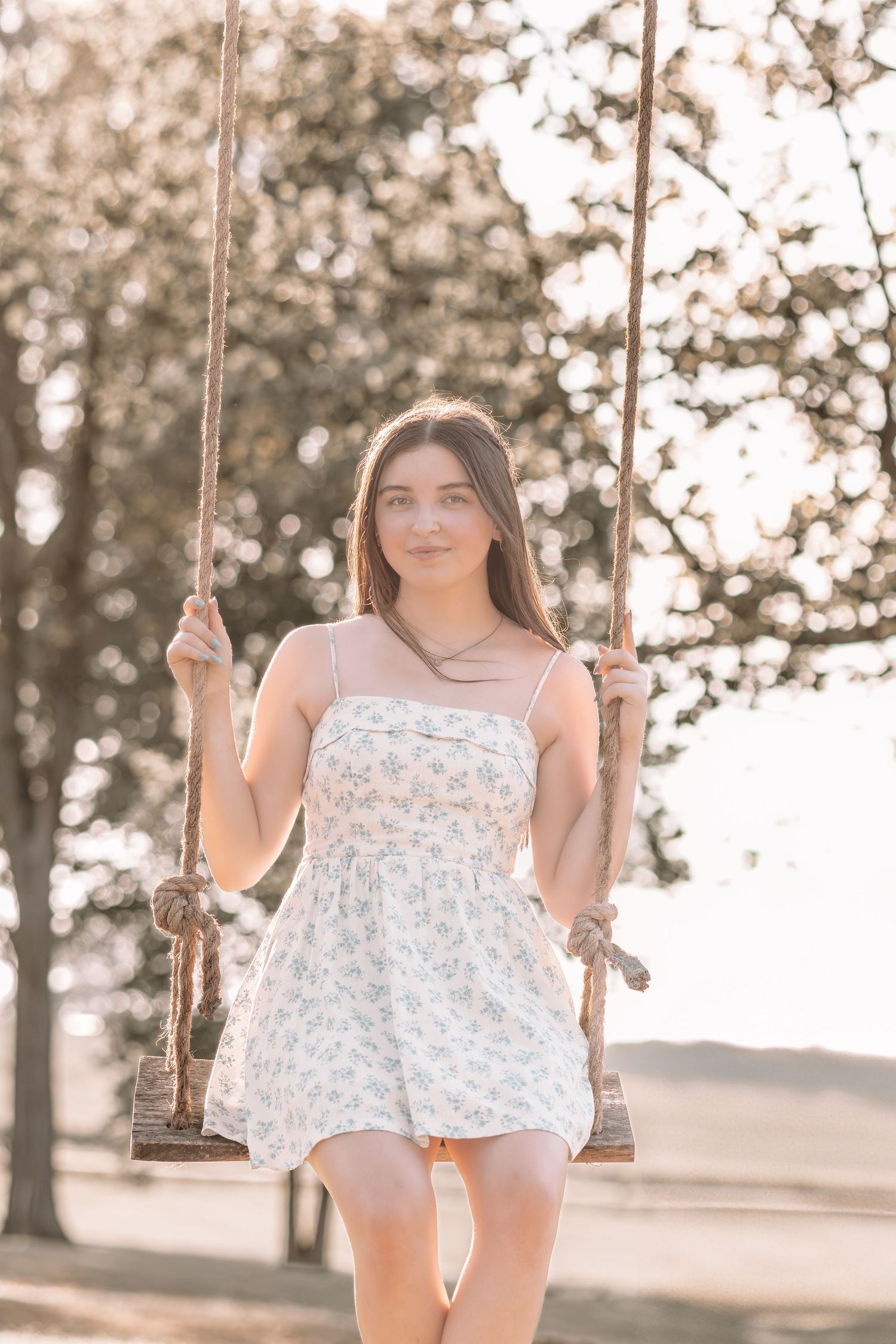 White floral dress captured on a rustic wooden swing in soft sunlight.