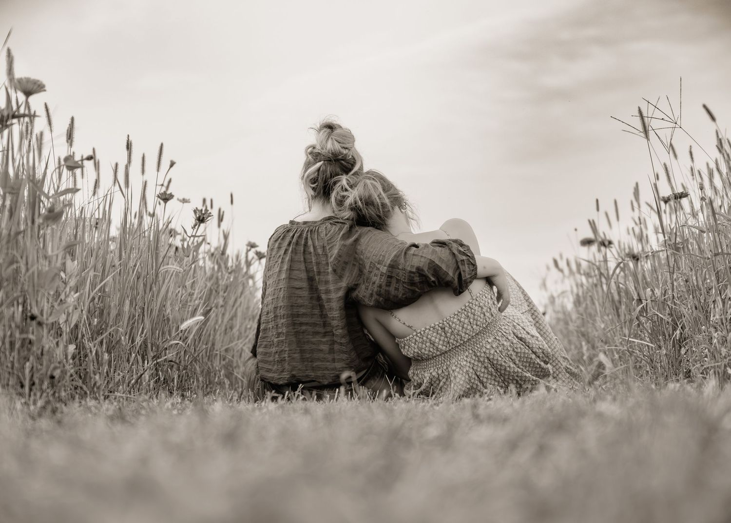 Two people sitting in a wildflower meadow, embracing each other from behind in a serene black and white photo.