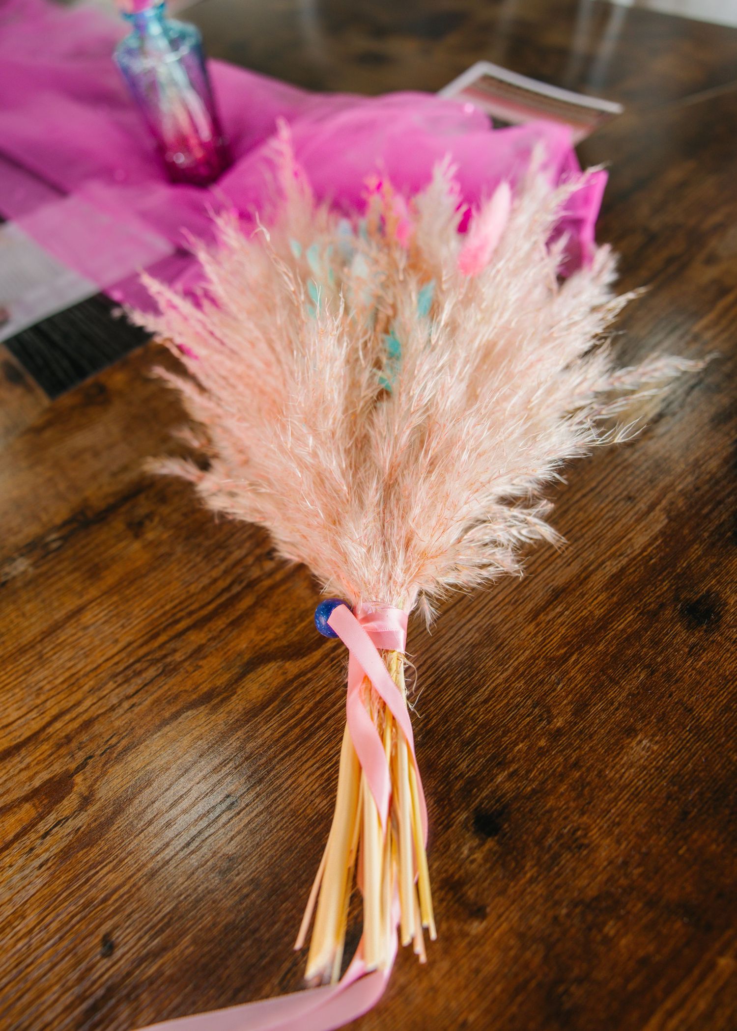 Dried pampas grass bouquet tied with colorful pink and blue ribbons on a wooden table.