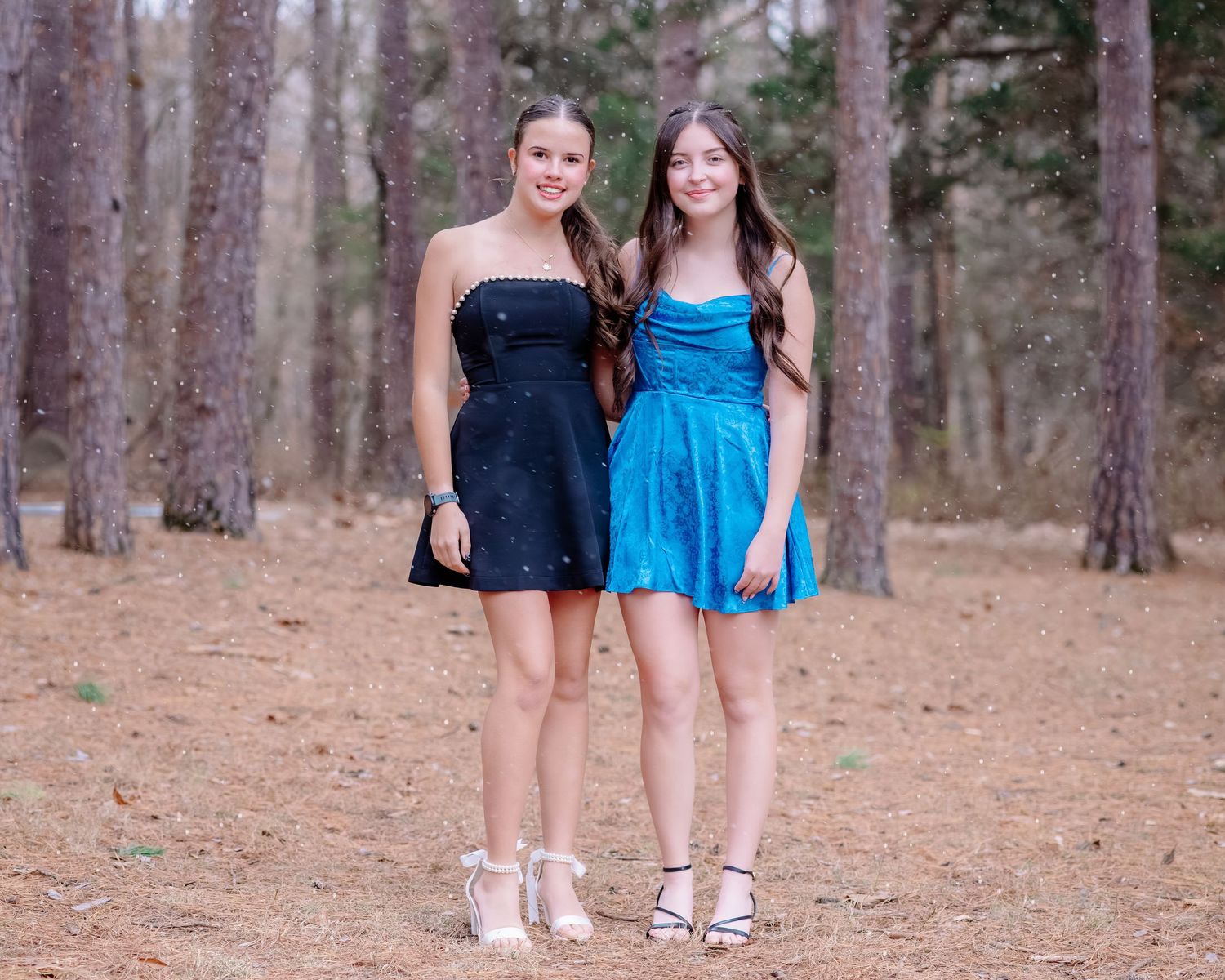 Two people in coordinated blue and black outfits stand together in a pine forest setting.