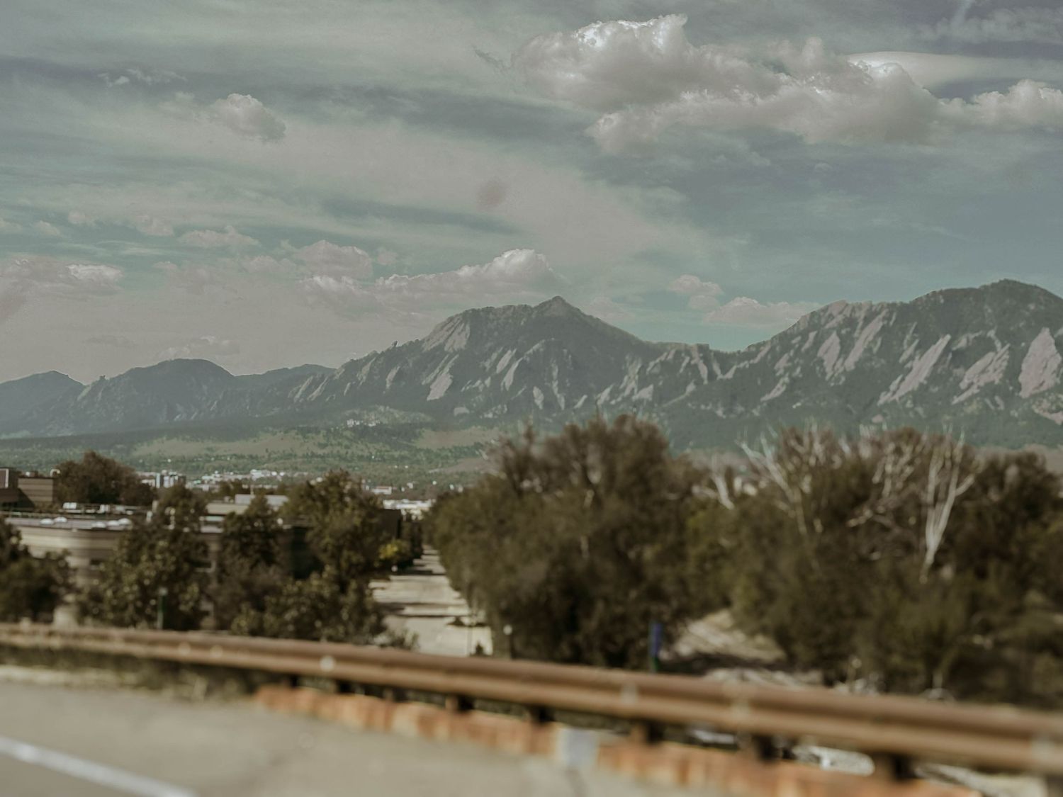 Scenic view of the Flatirons mountain range in Boulder, Colorado with dramatic cloudy sky and trees in foreground.