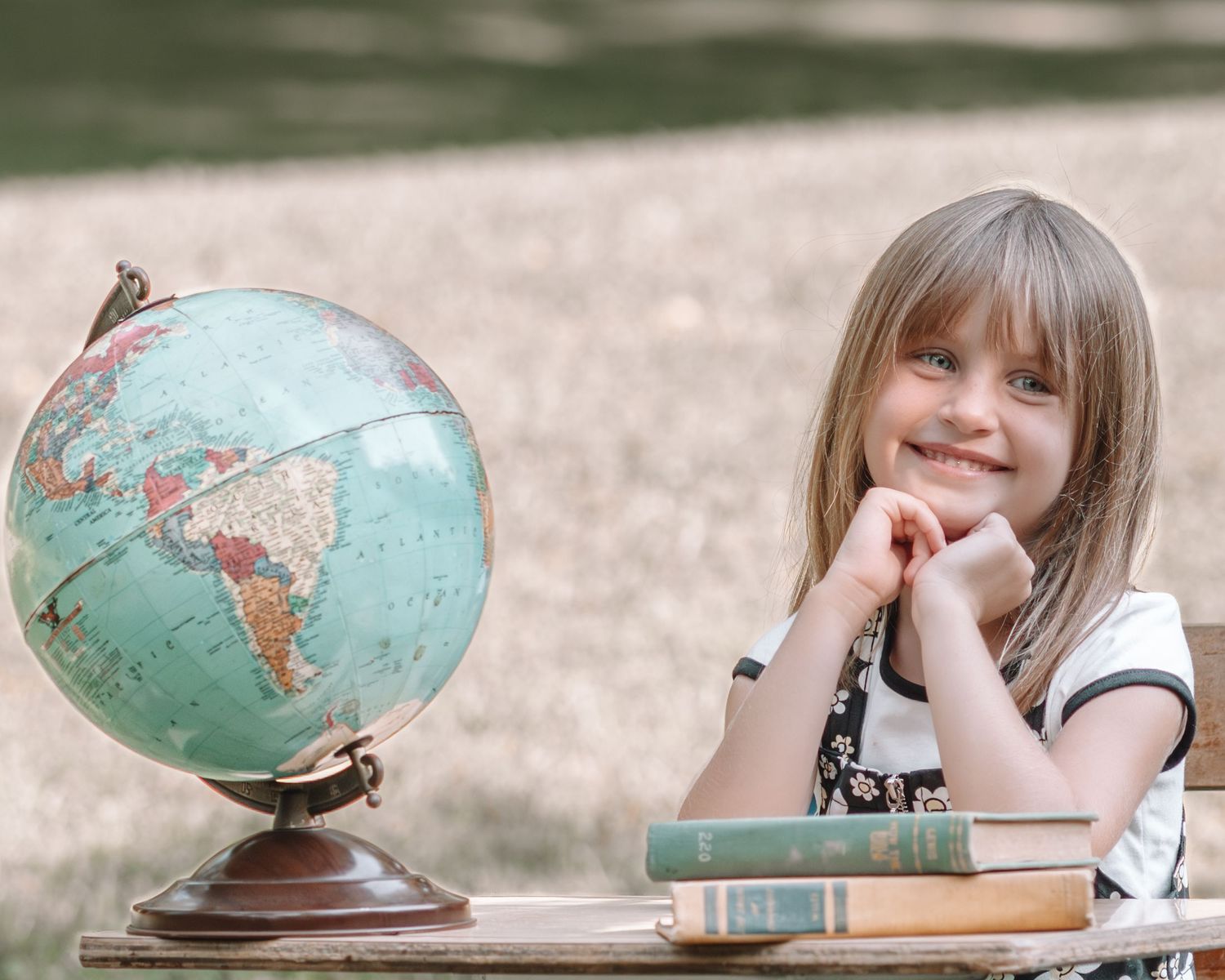 A person sits at a desk studying a vintage turquoise globe while taking notes in a journal.