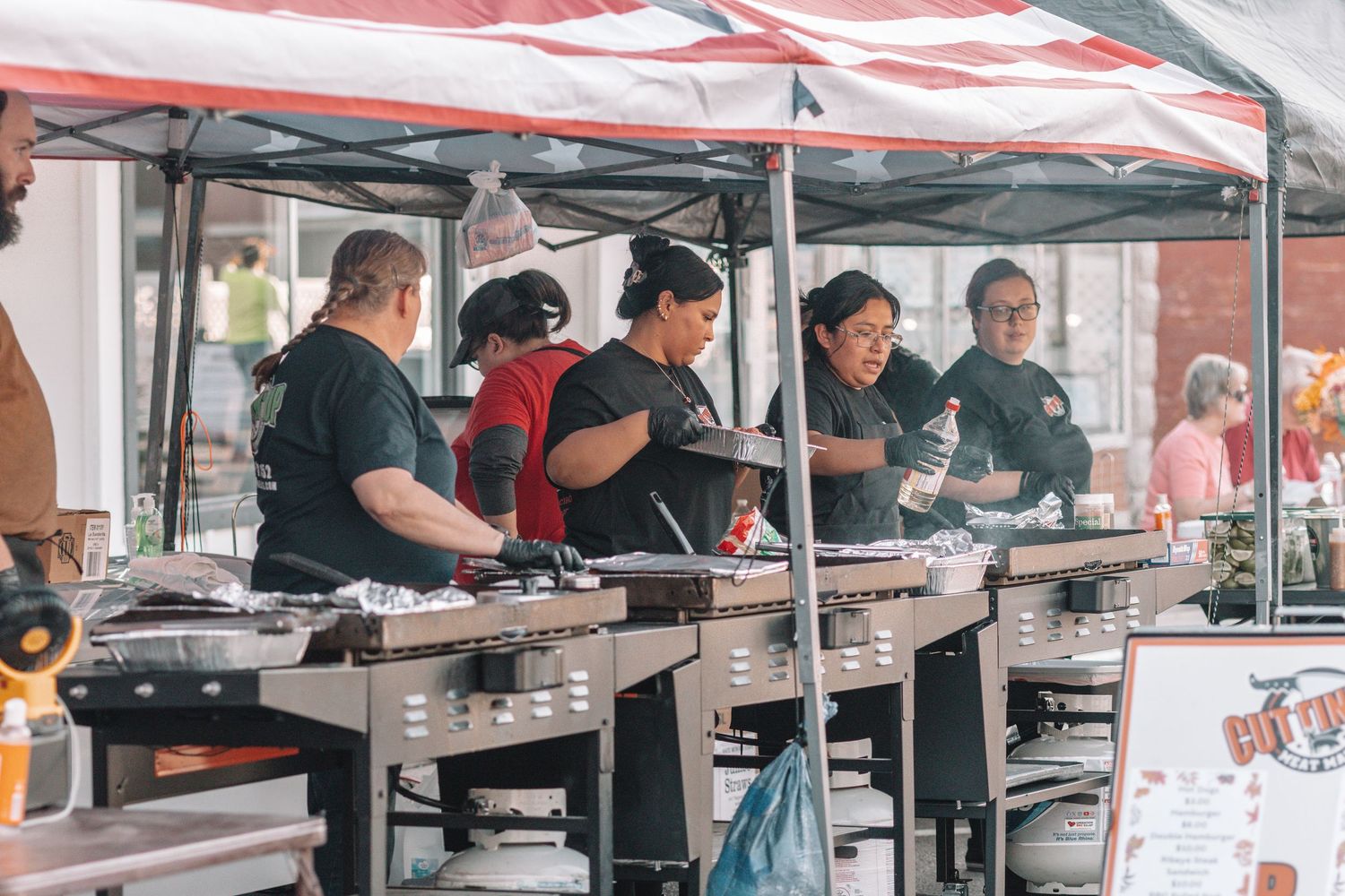 Row of food vendor tents with workers preparing meals at an outdoor festival.