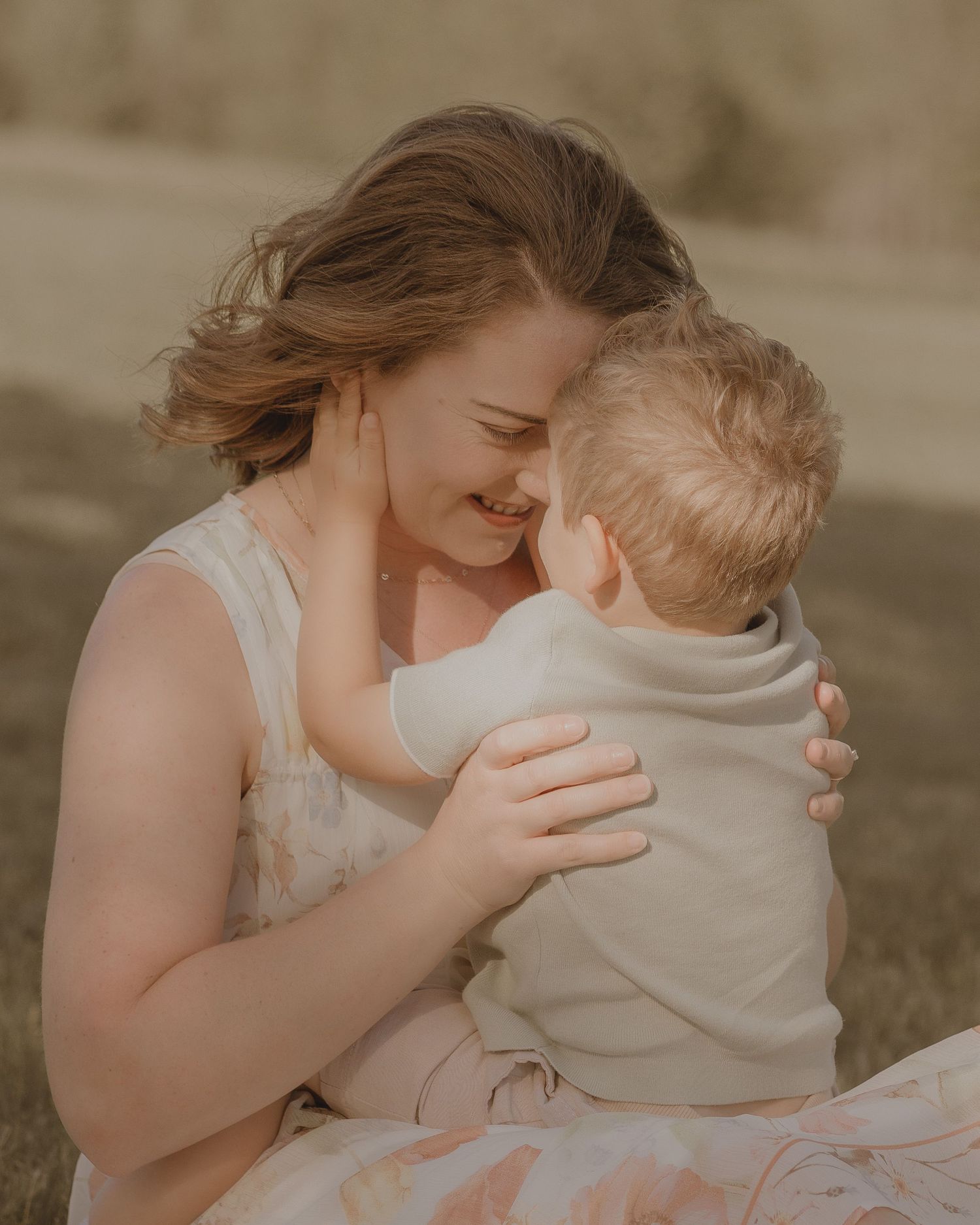 A smiling mother tenderly embraces her young toddler outdoors, sharing a sweet moment of love and connection.