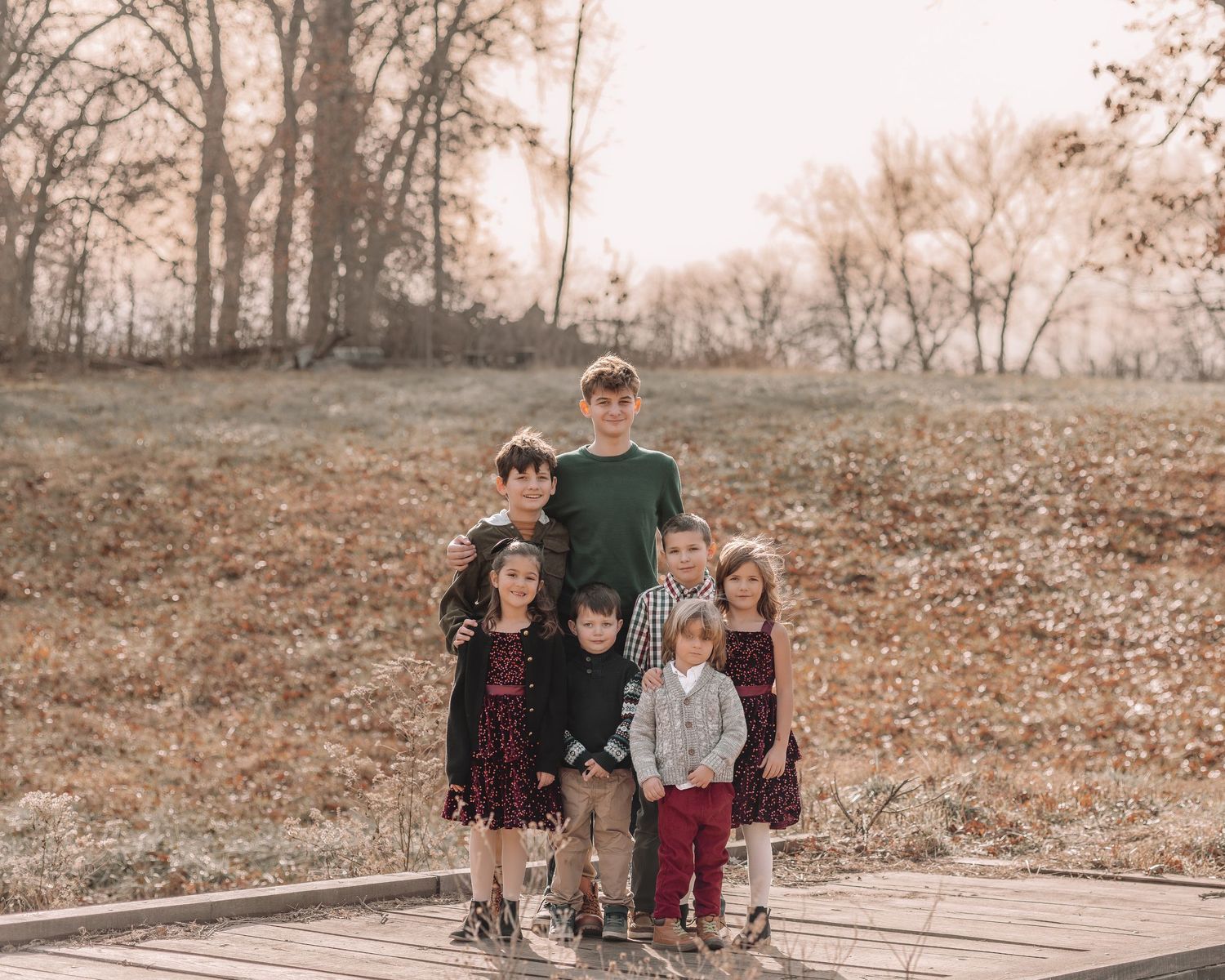 A family portrait taken outdoors on a wooden deck with autumn trees in the background.