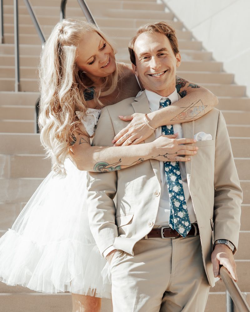 A couple in wedding attire share intimate embraces while posing on a staircase in natural light.