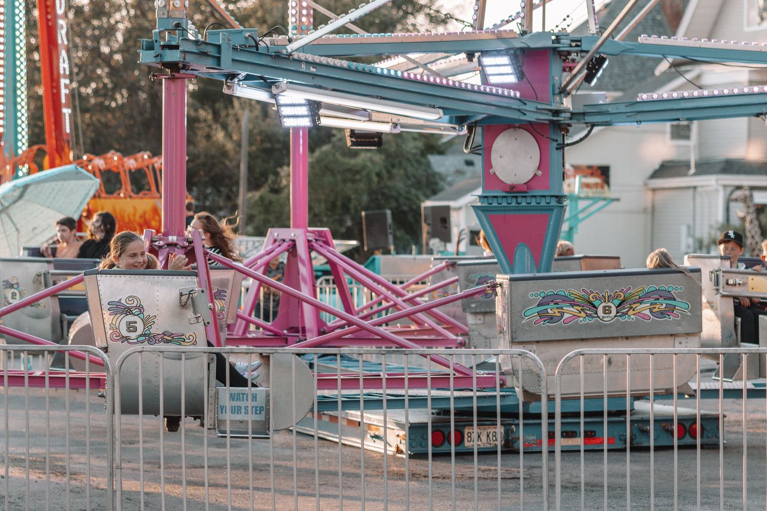 Colorful carnival rides and attractions with metal barriers at dusk.