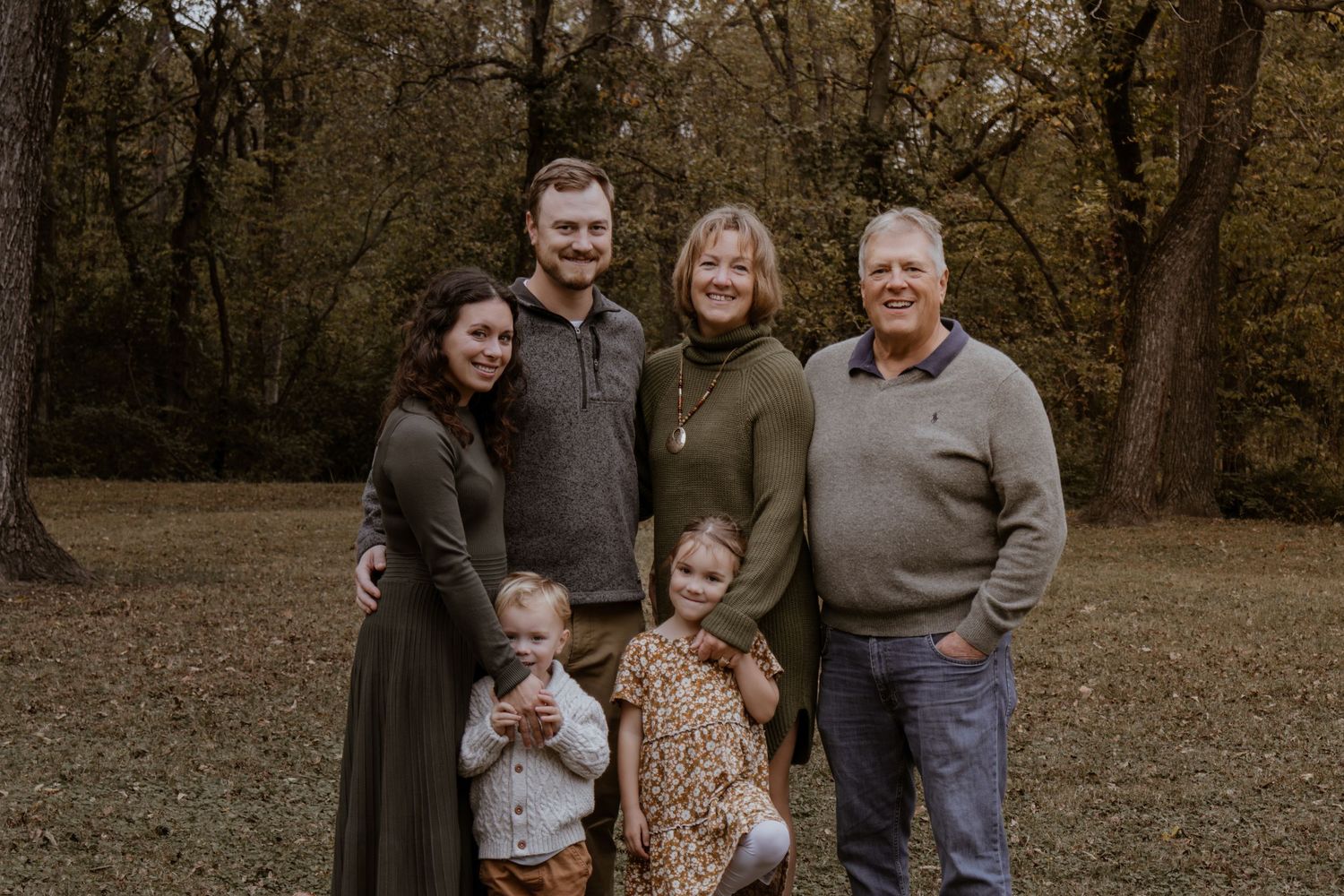 Multi-generational family group poses together in a wooded setting during fall.