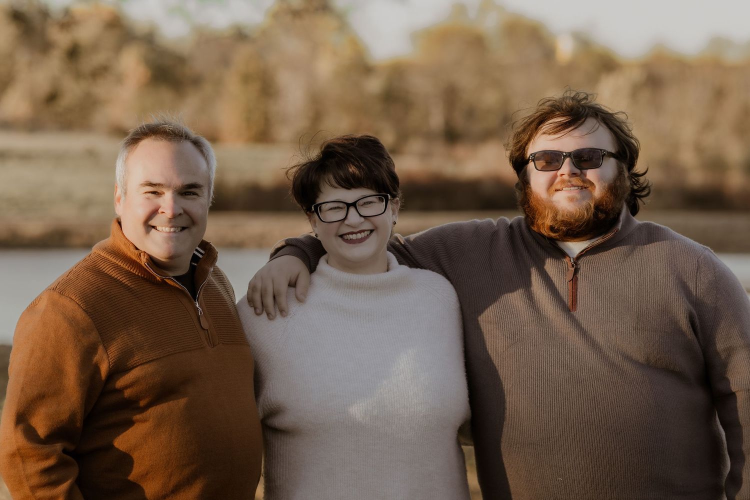 A group of people stand close together against a warm sunset backdrop creating a casual outdoor portrait.