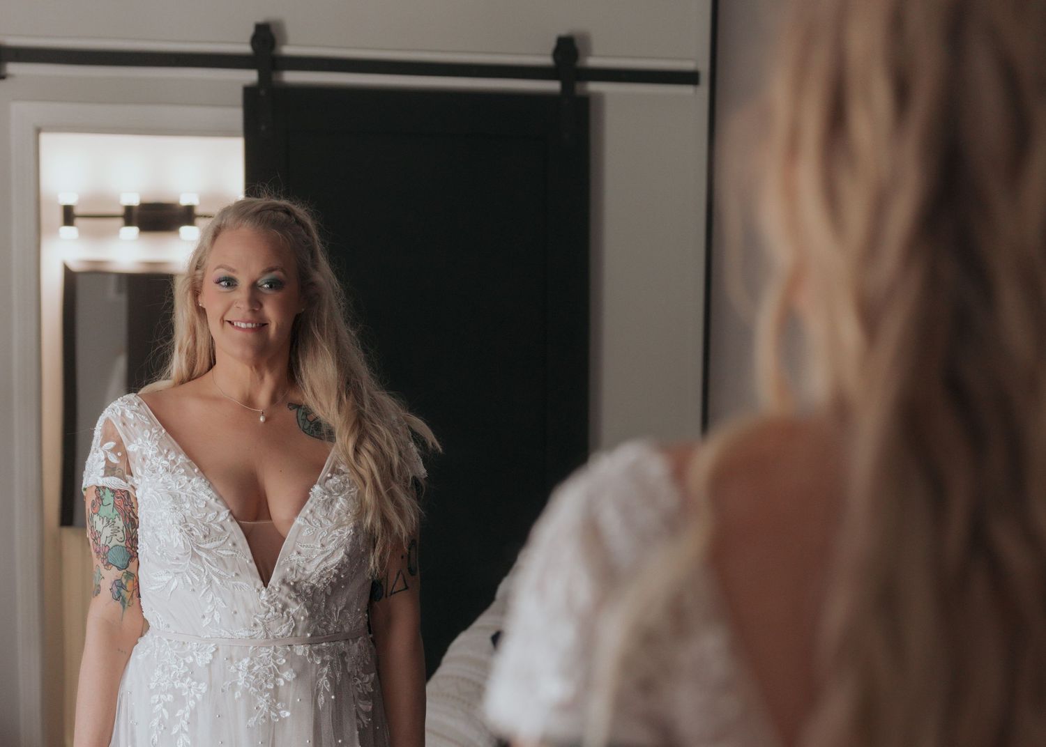 Blonde bride in lace wedding gown admiring herself in a mirror with barn door backdrop.