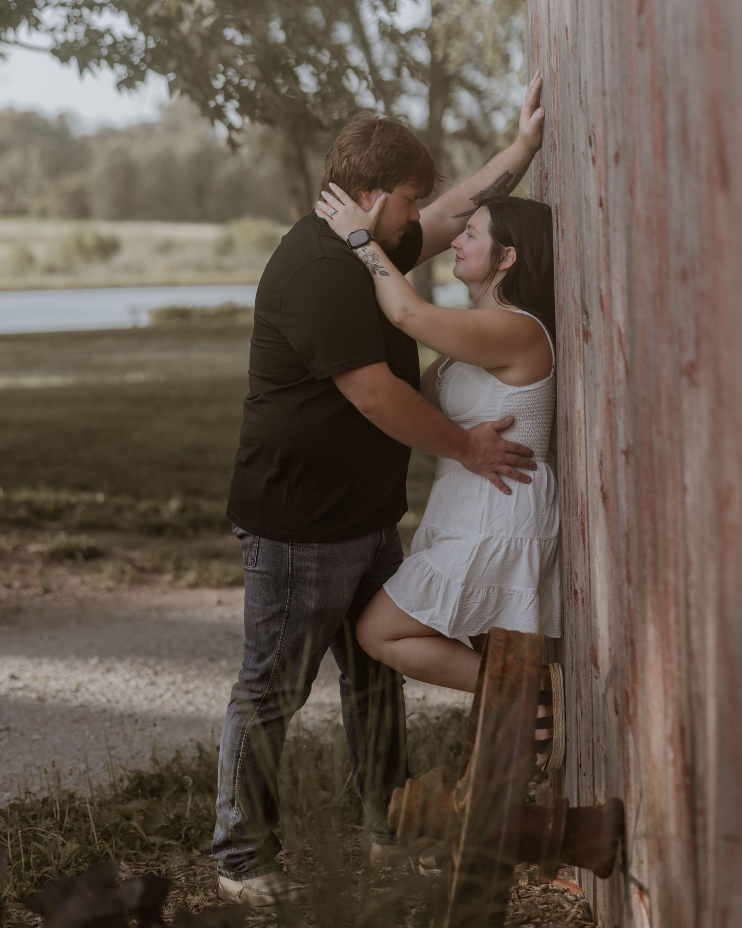 Romantic couple sharing an intimate moment leaning against a rustic barn wall surrounded by lush greenery.