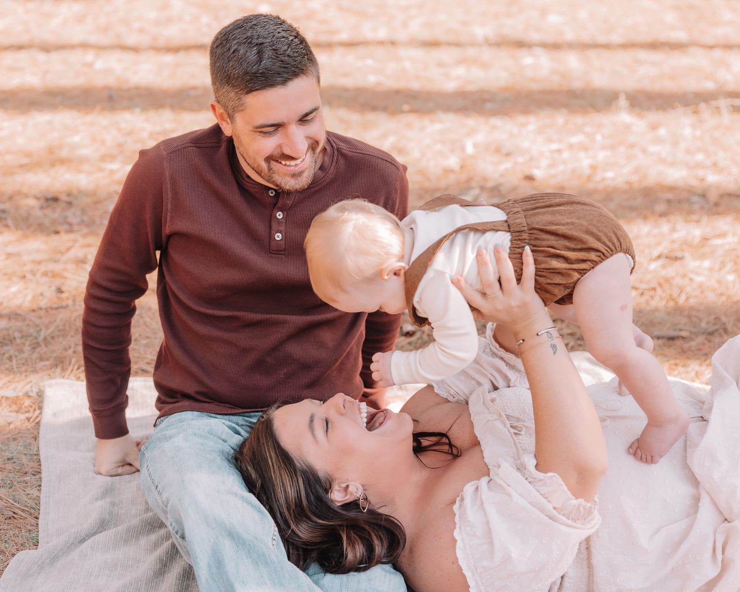 A joyful family shares laughter while relaxing on a blanket in the woods.