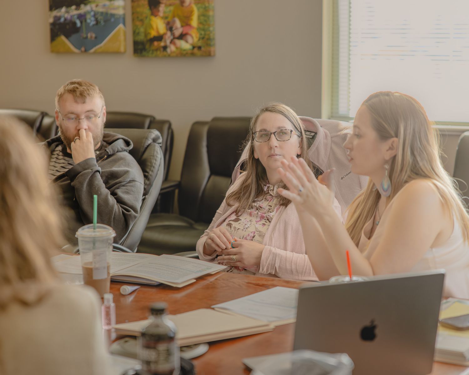 Professionals engaged in a business meeting around a conference table with laptops and drinks in a modern office.