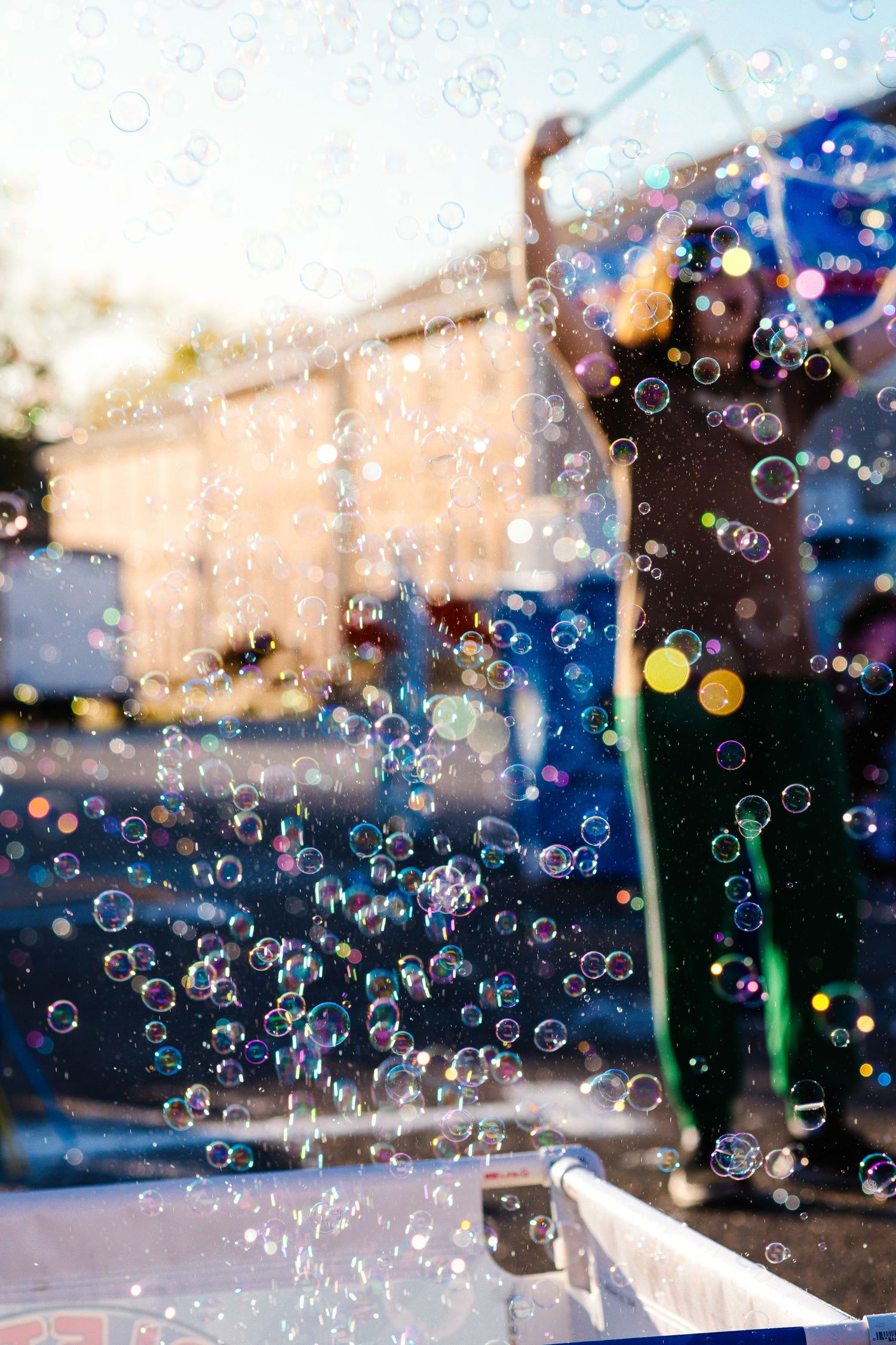 Colorful soap bubbles floating in the air against a blurred urban background on a sunny day.