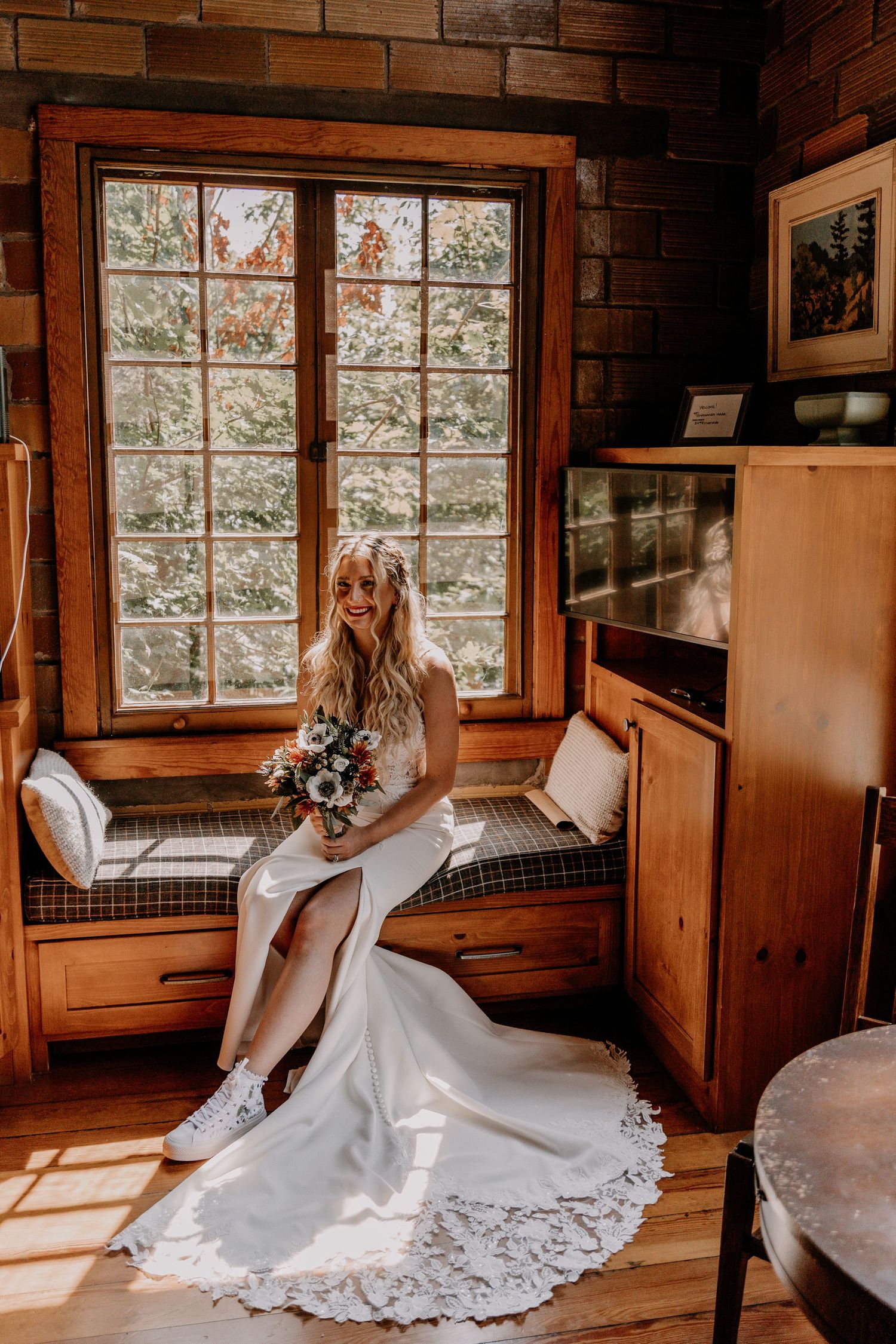 A white wedding dress flowing in natural light from wooden cabin windows creates a dreamy bridal scene.