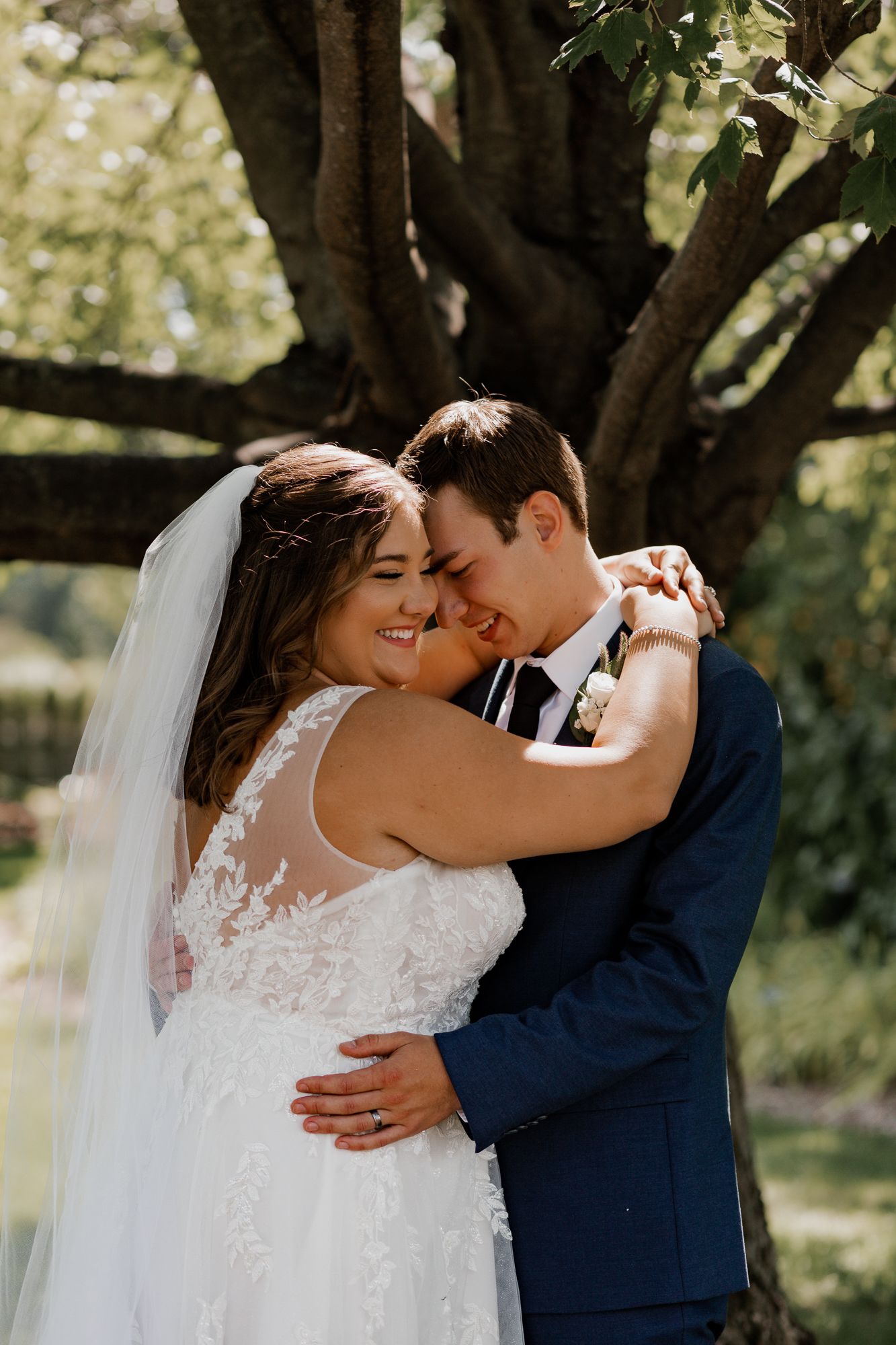 Sun-lit wedding portrait of couple embracing under a large tree.