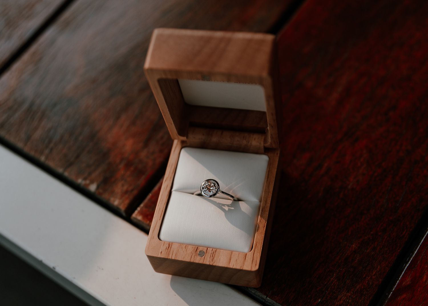 Engagement ring in wooden box displayed on dark wooden surface.