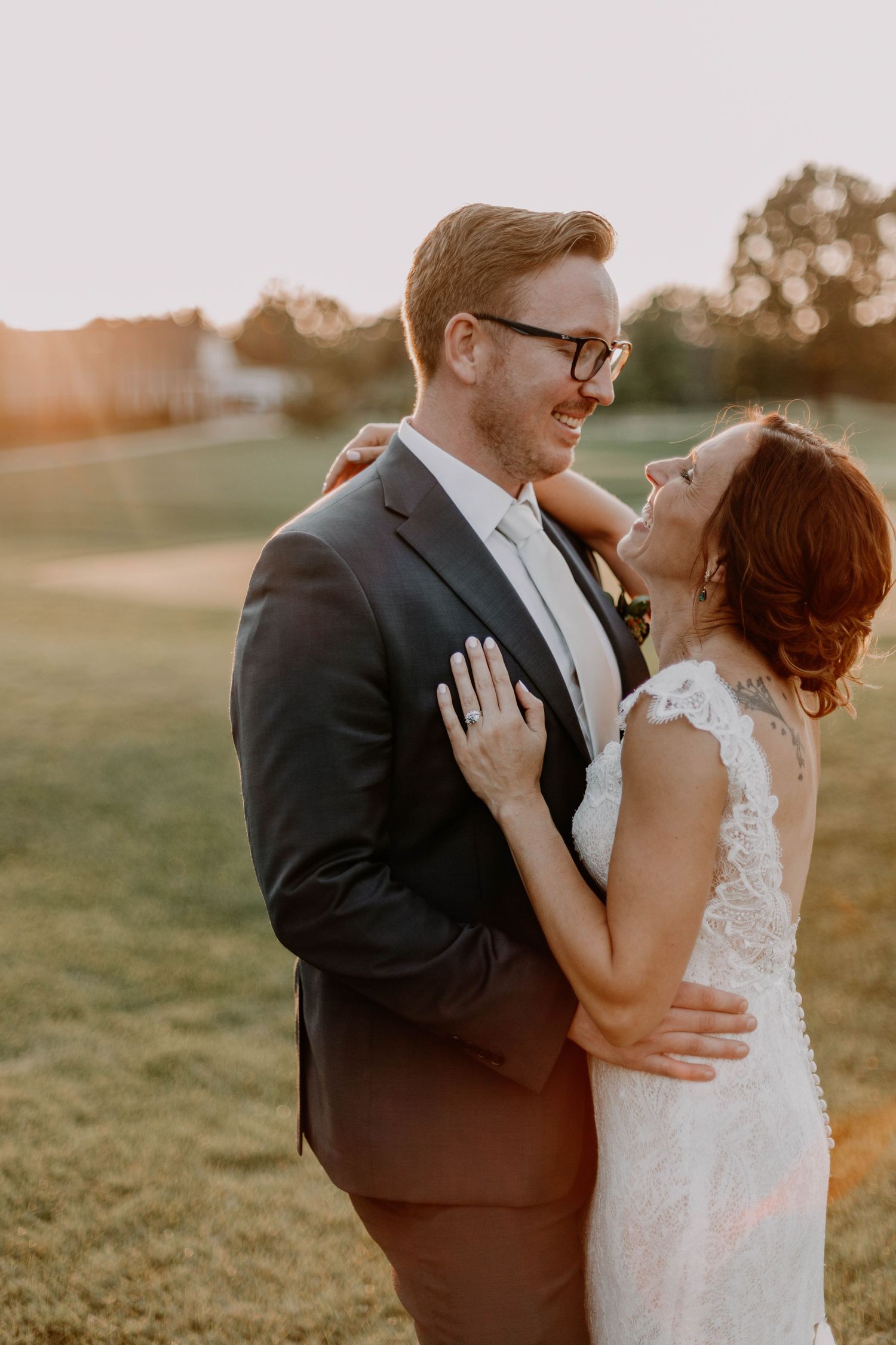 A couple shares a candid laugh during their sunset wedding portraits on a grassy hill.