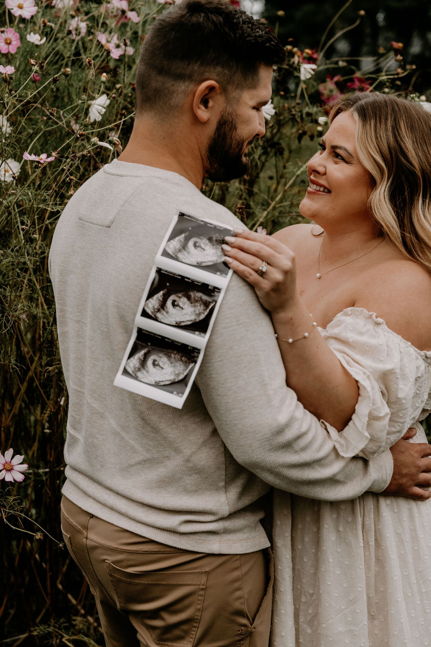 Couple holding ultrasound photos while embracing in a flower field.