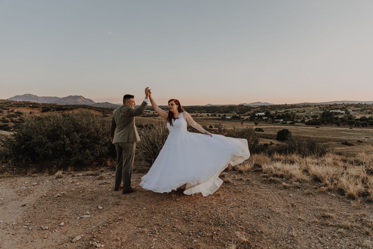 Wedding couple embracing on a desert hilltop during golden hour with mountains in the background.
