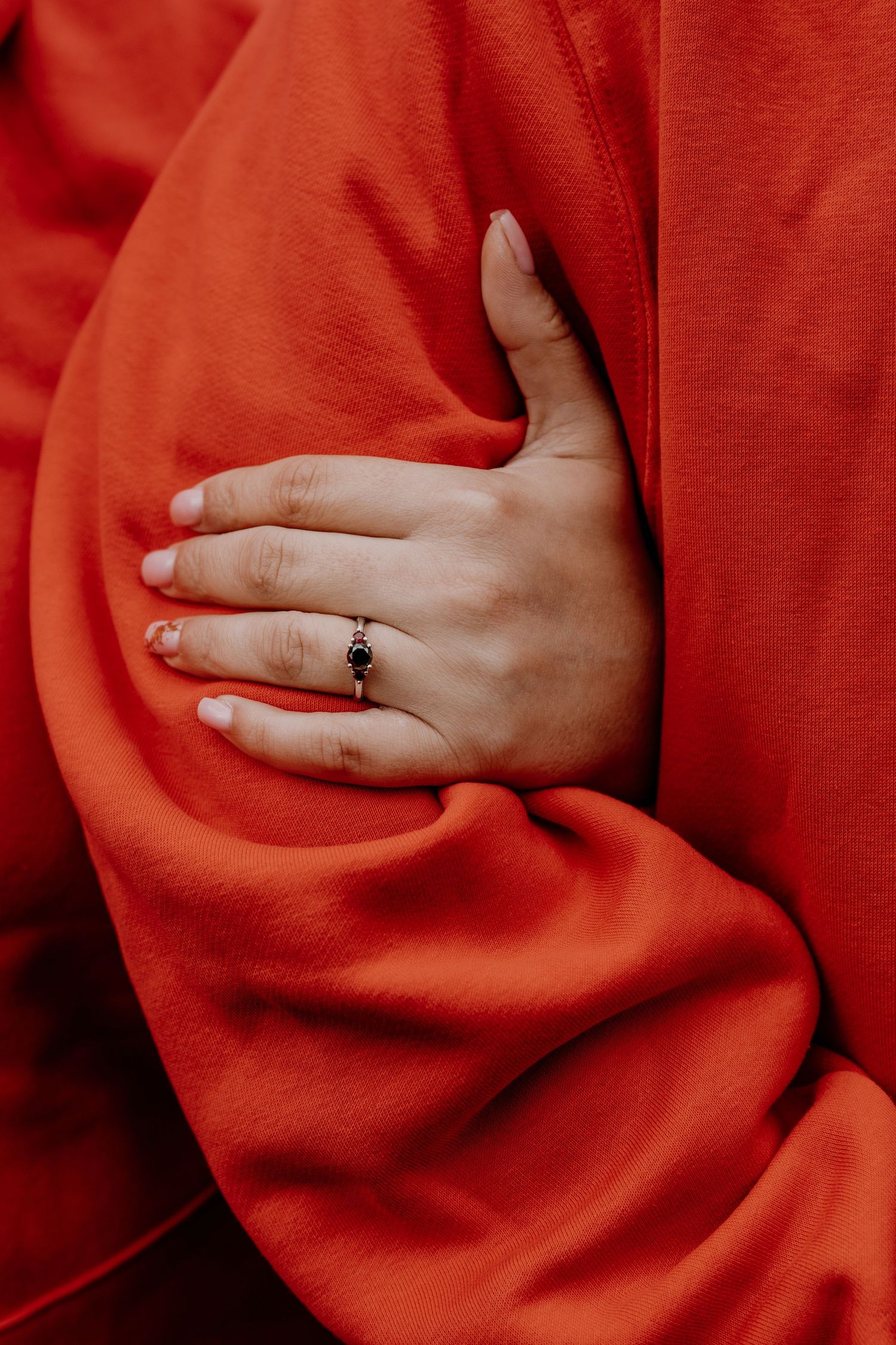 Close-up of a hand with an engagement ring against bright red fabric.