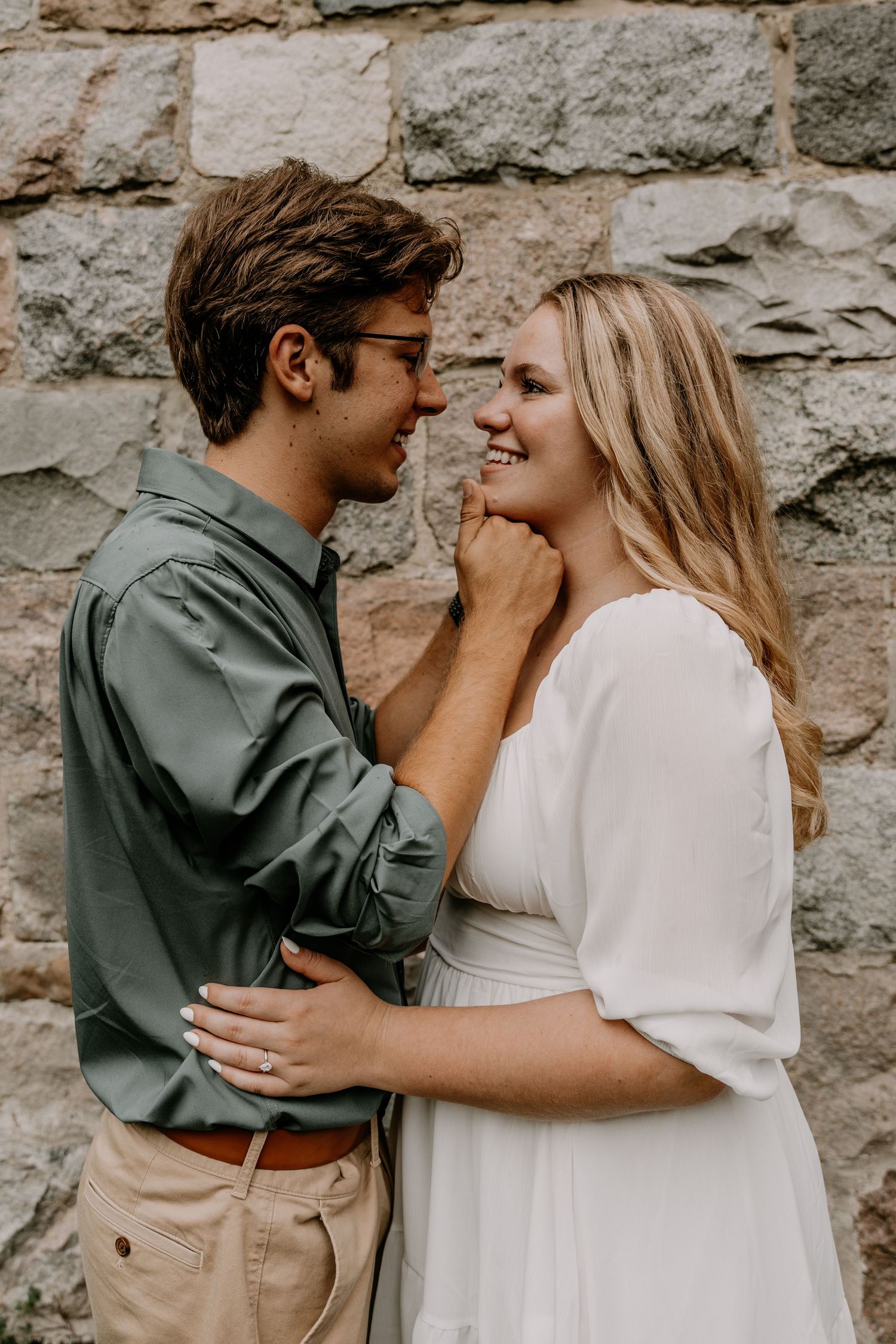 A couple shares an intimate moment while posing against a stone wall outdoors.