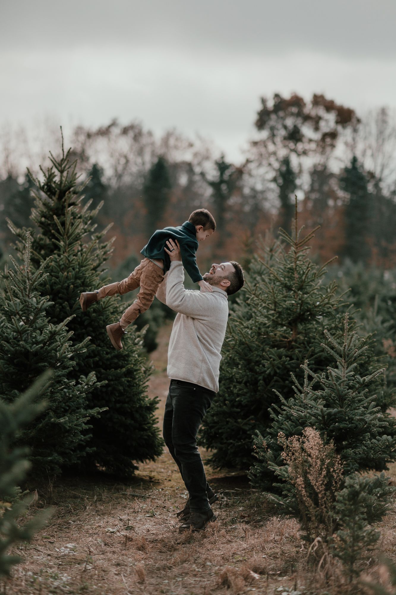 Playful moment at a Christmas tree farm with someone lifting a child into the air.