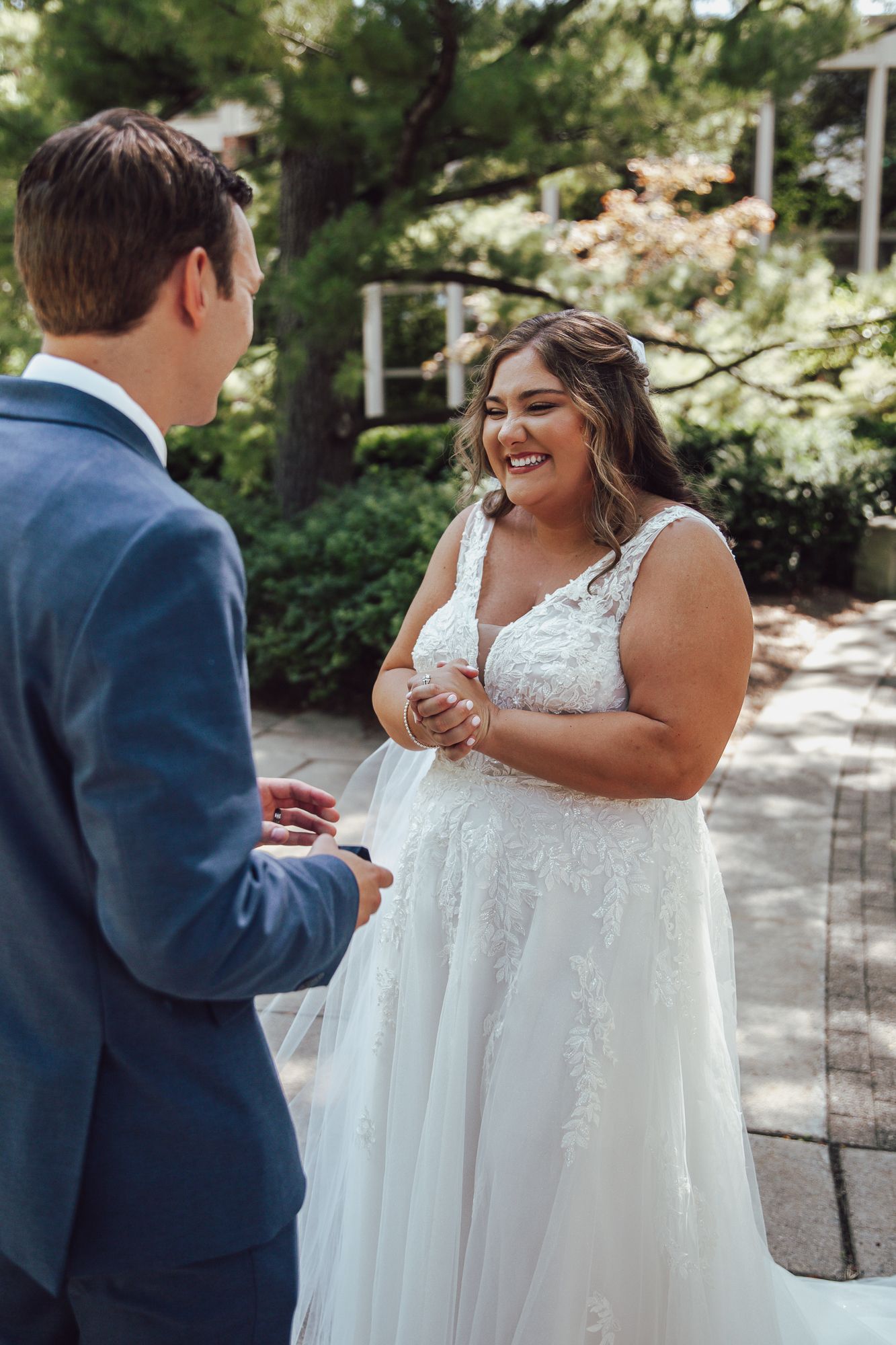 Joyful bride in a lace wedding dress shares a candid moment with her groom on a garden pathway.