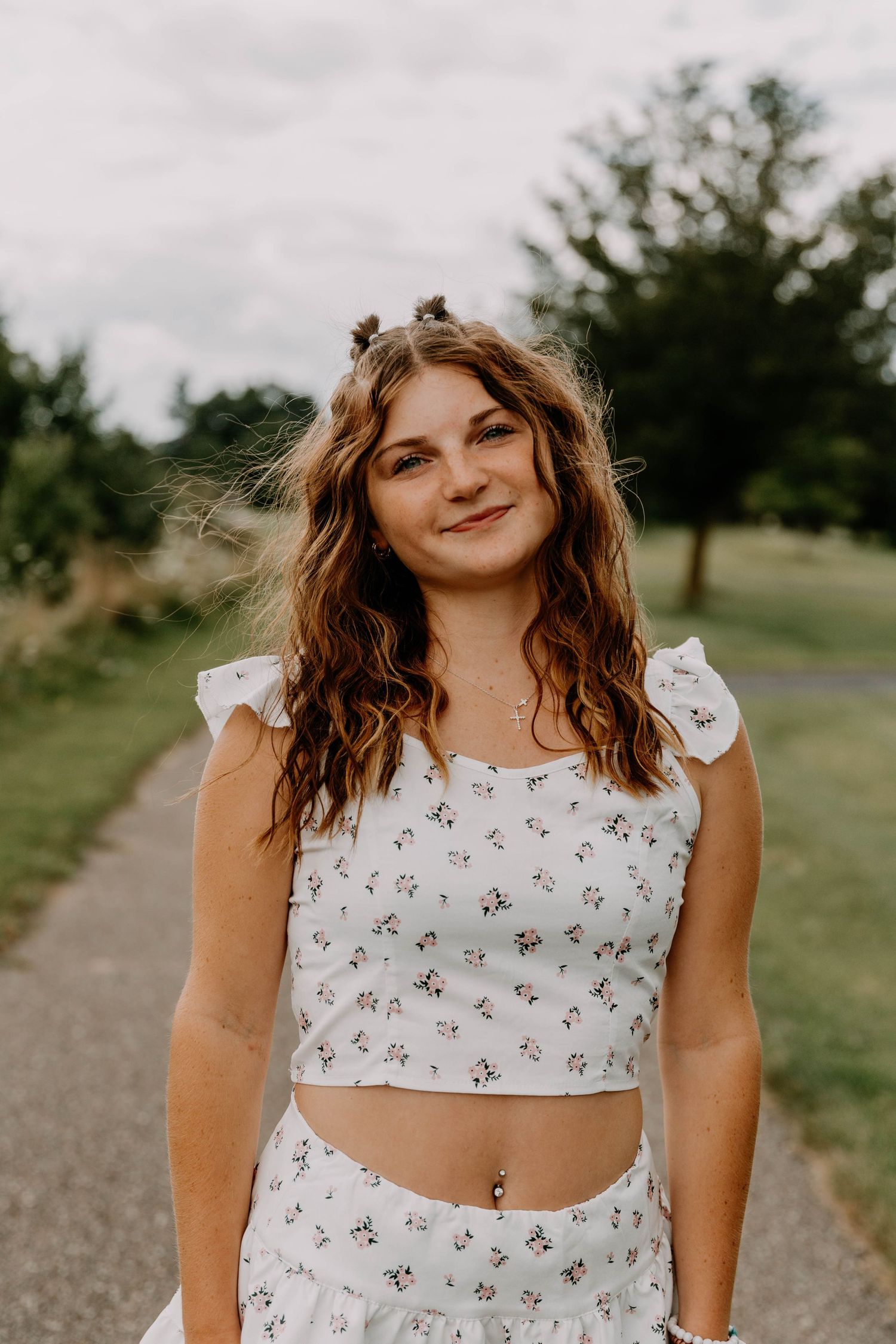 Person in white floral crop top set poses outdoors on country path.