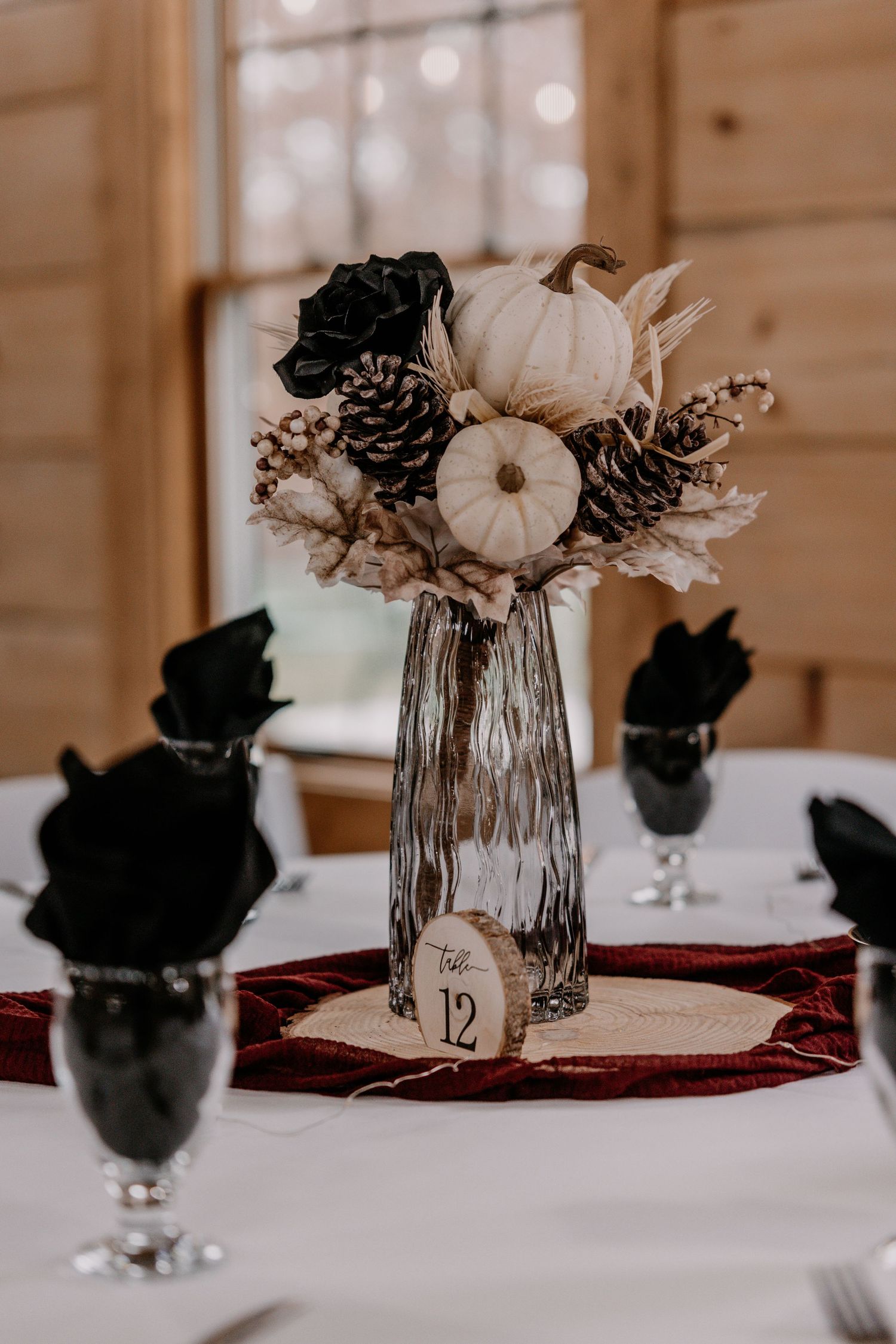 Elegant fall wedding centerpiece with white pumpkins and pinecones in textured glass vase.