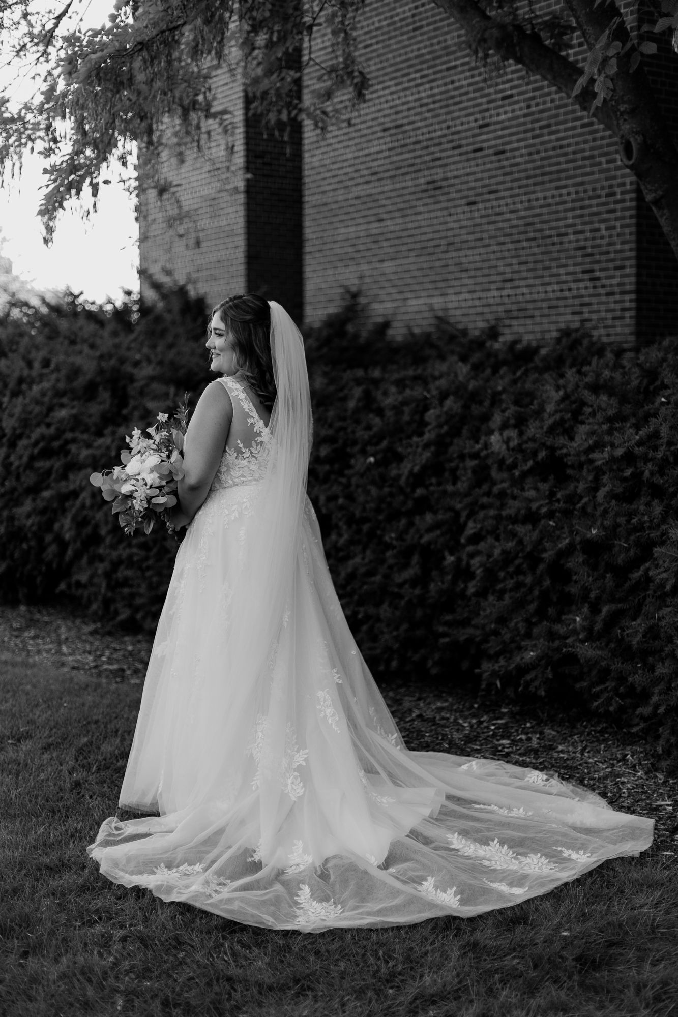 Black and white bridal portrait showing detailed lace wedding dress with long train.