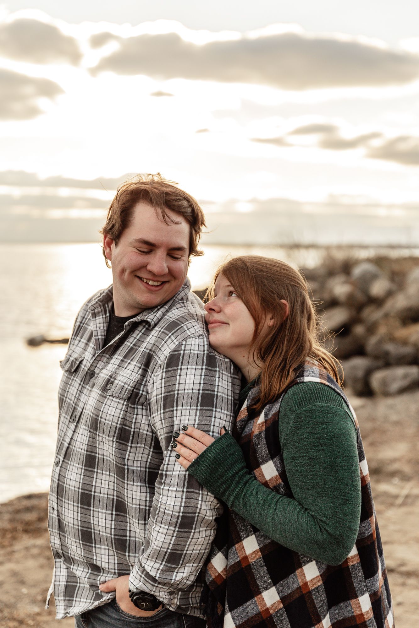 A couple shares a tender moment while laughing together on a coastal shoreline.
