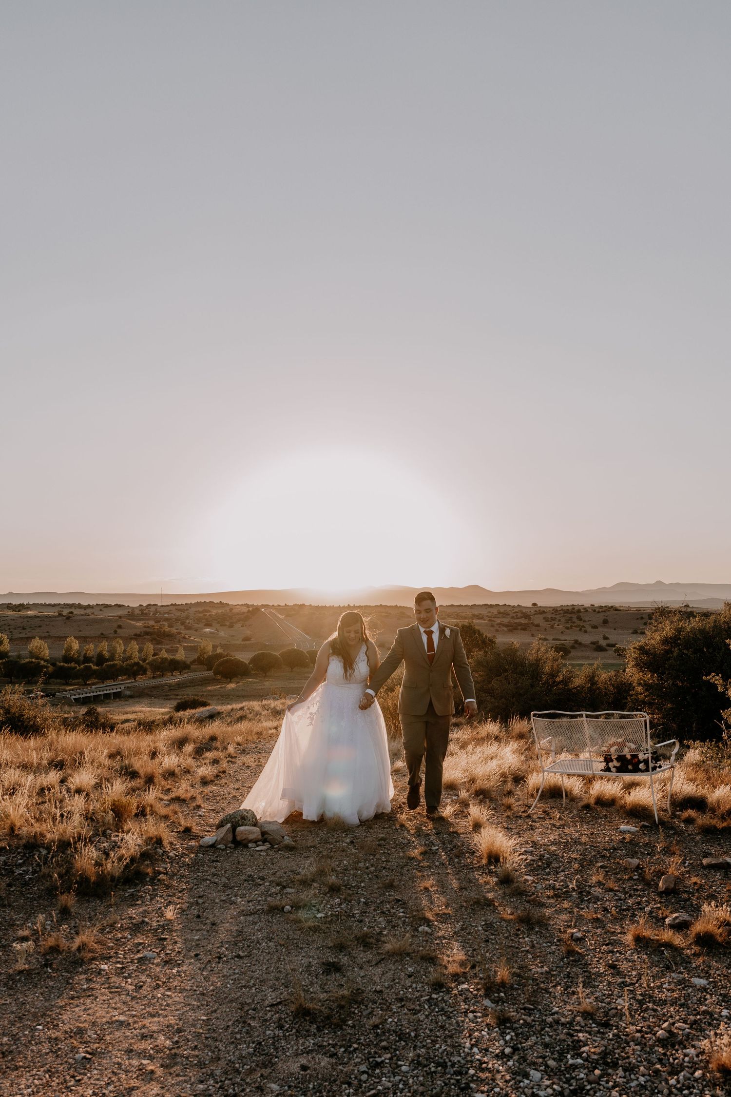 Wedding couple silhouetted against dramatic desert sunset landscape.