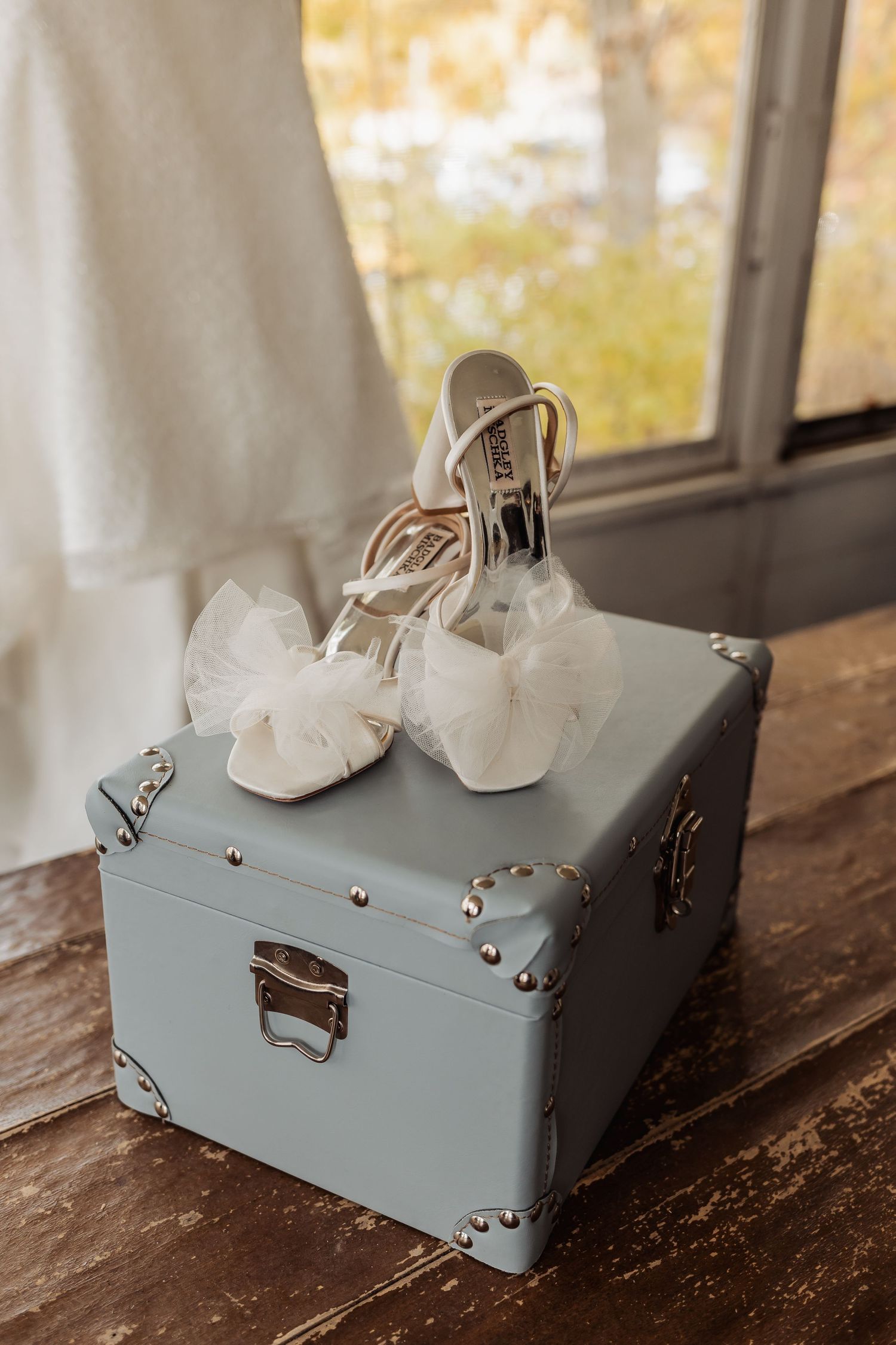 A pale blue vintage suitcase sits on a rustic wooden surface near a sunlit window.